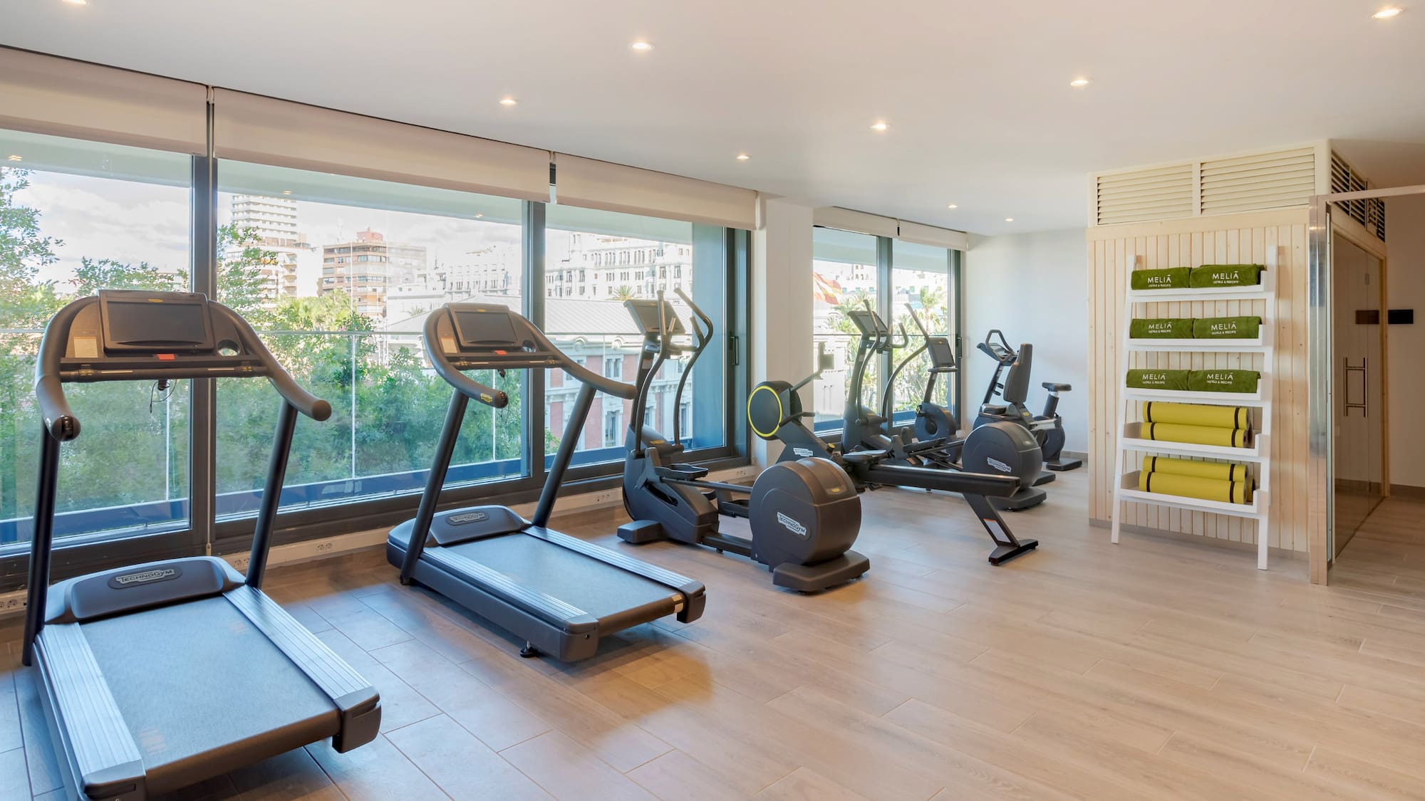 Moderno gimnasio Meliá con máquinas de ejercicio y vista a la ciudad.