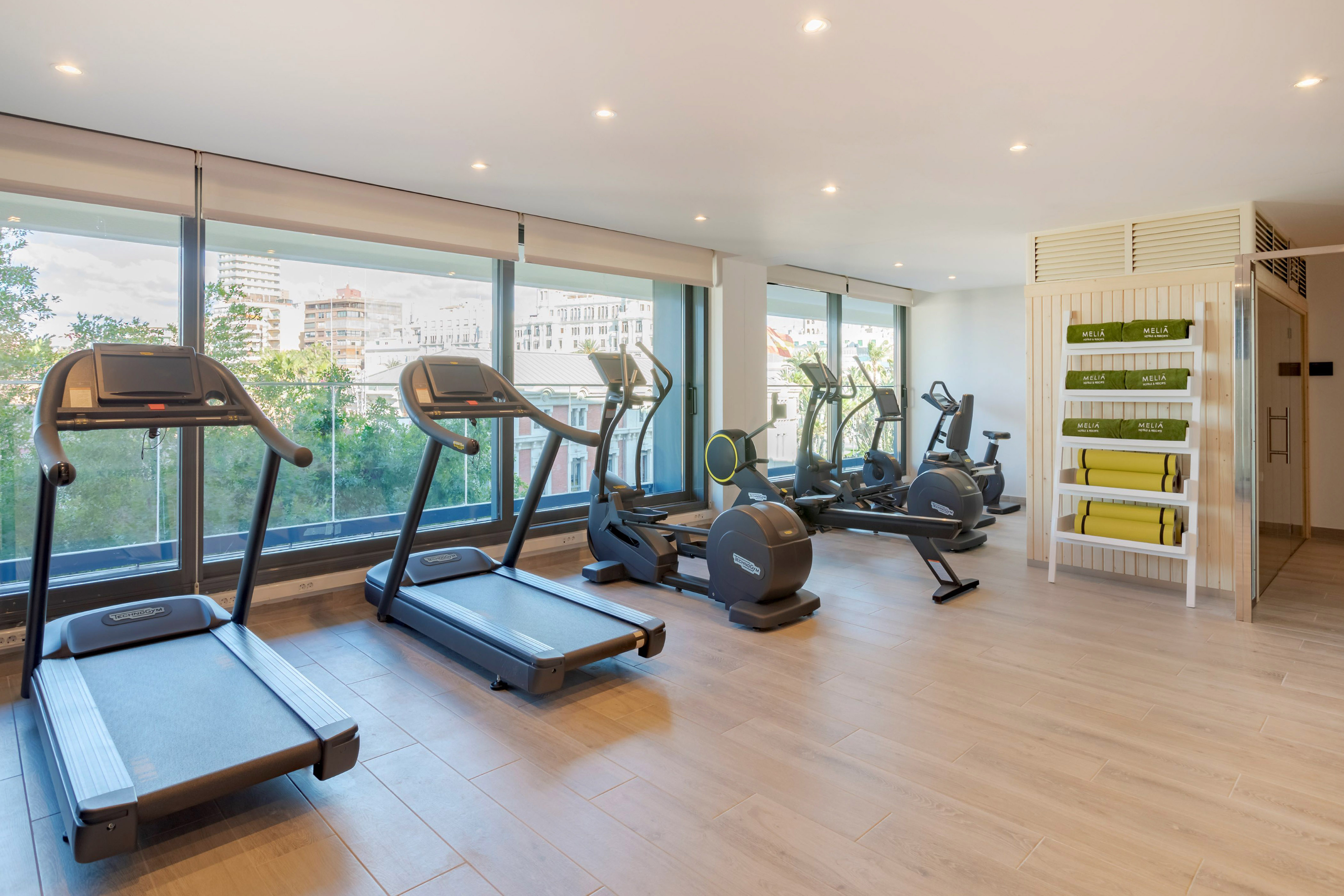 Moderno gimnasio Meliá con máquinas de ejercicio y vista a la ciudad.