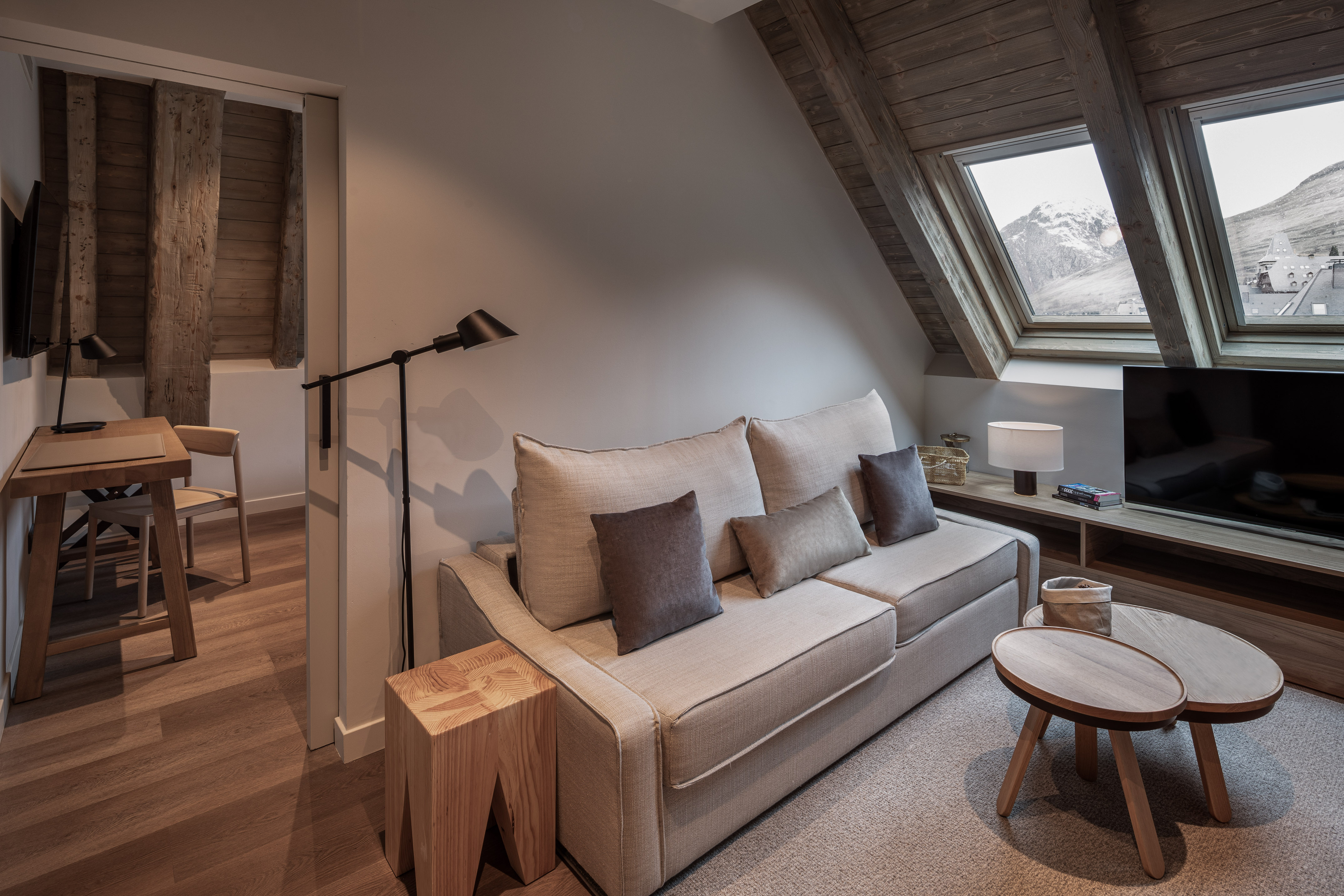 Cozy hotel living room with sofa, wood accents, and snowy mountain view.