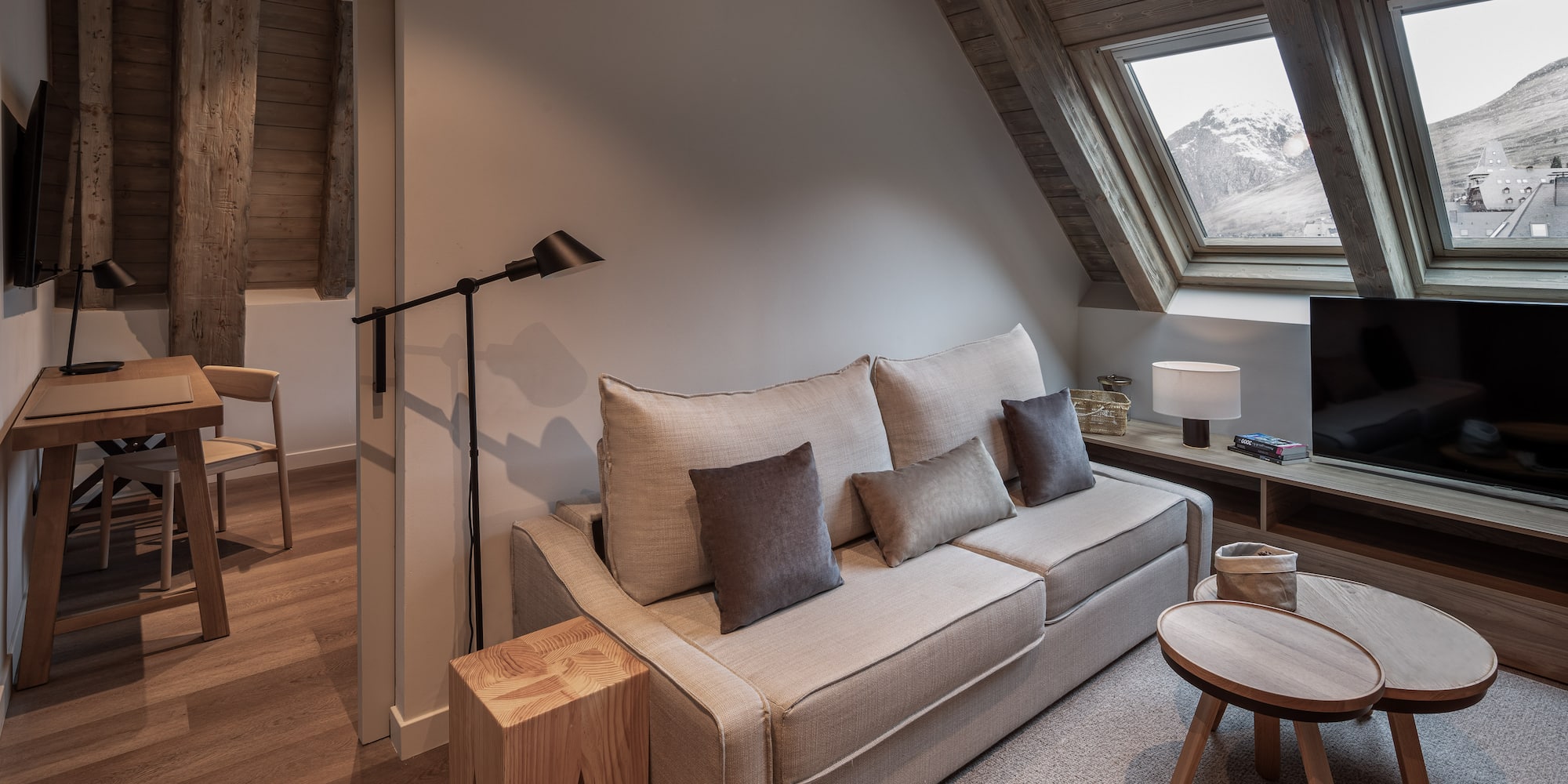 Cozy hotel living room with sofa, wood accents, and snowy mountain view.
