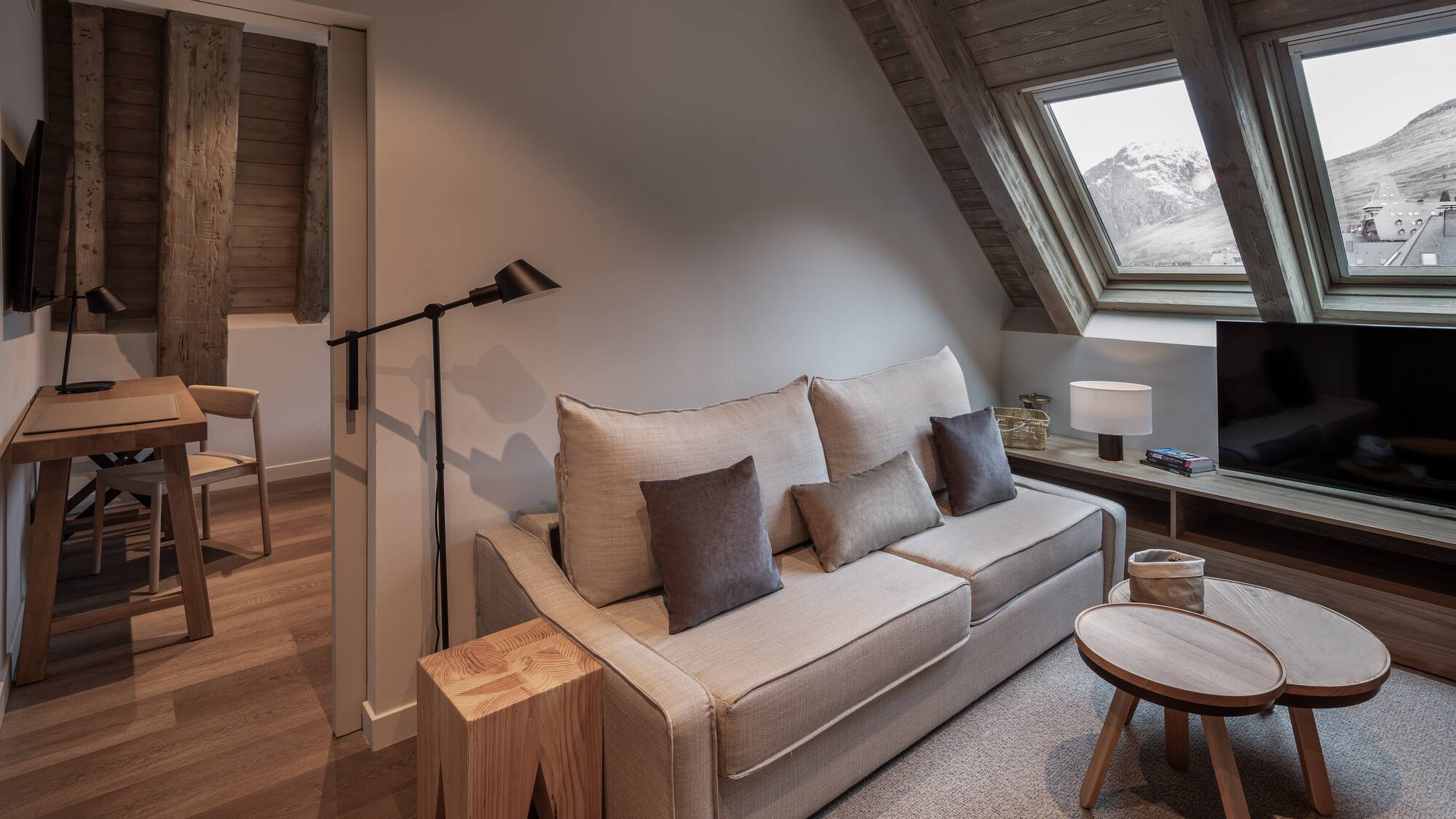 Cozy hotel living room with sofa, wood accents, and snowy mountain view.