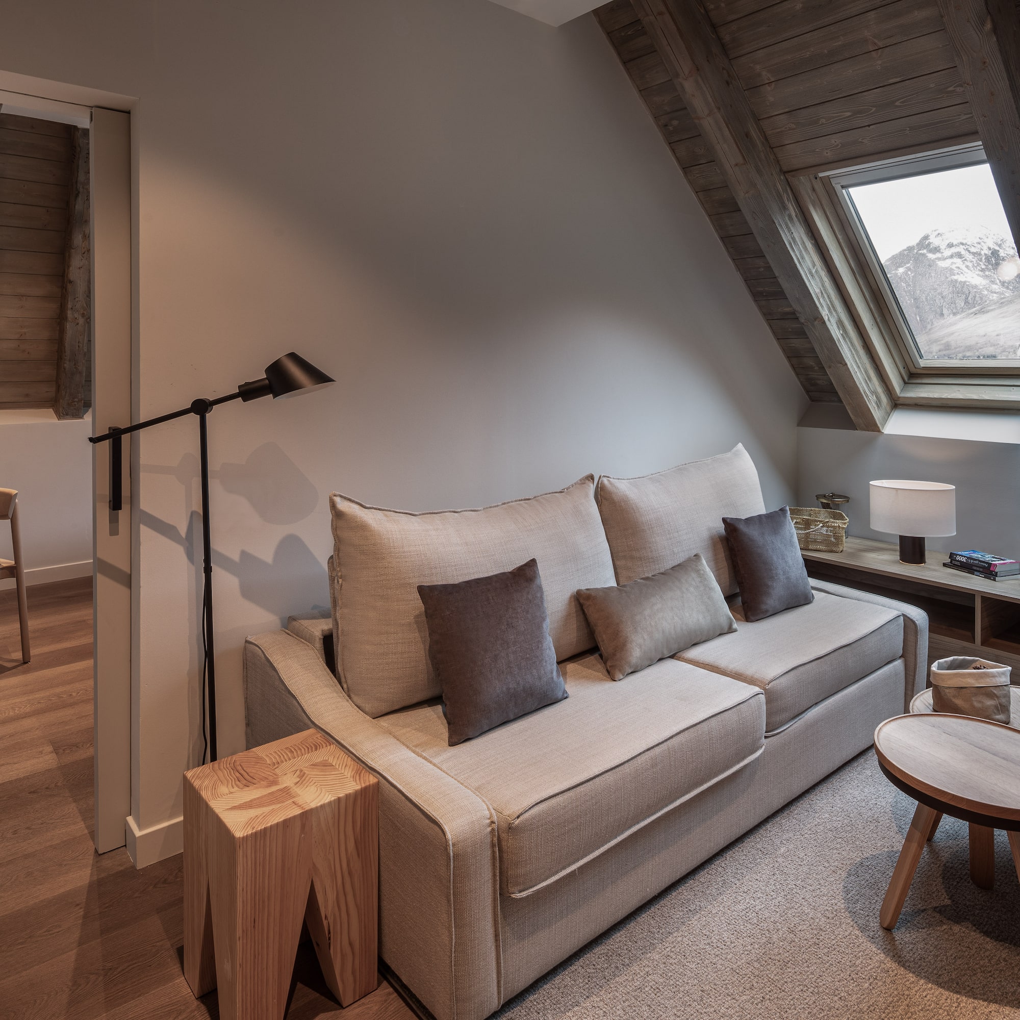 Cozy hotel living room with sofa, wood accents, and snowy mountain view.