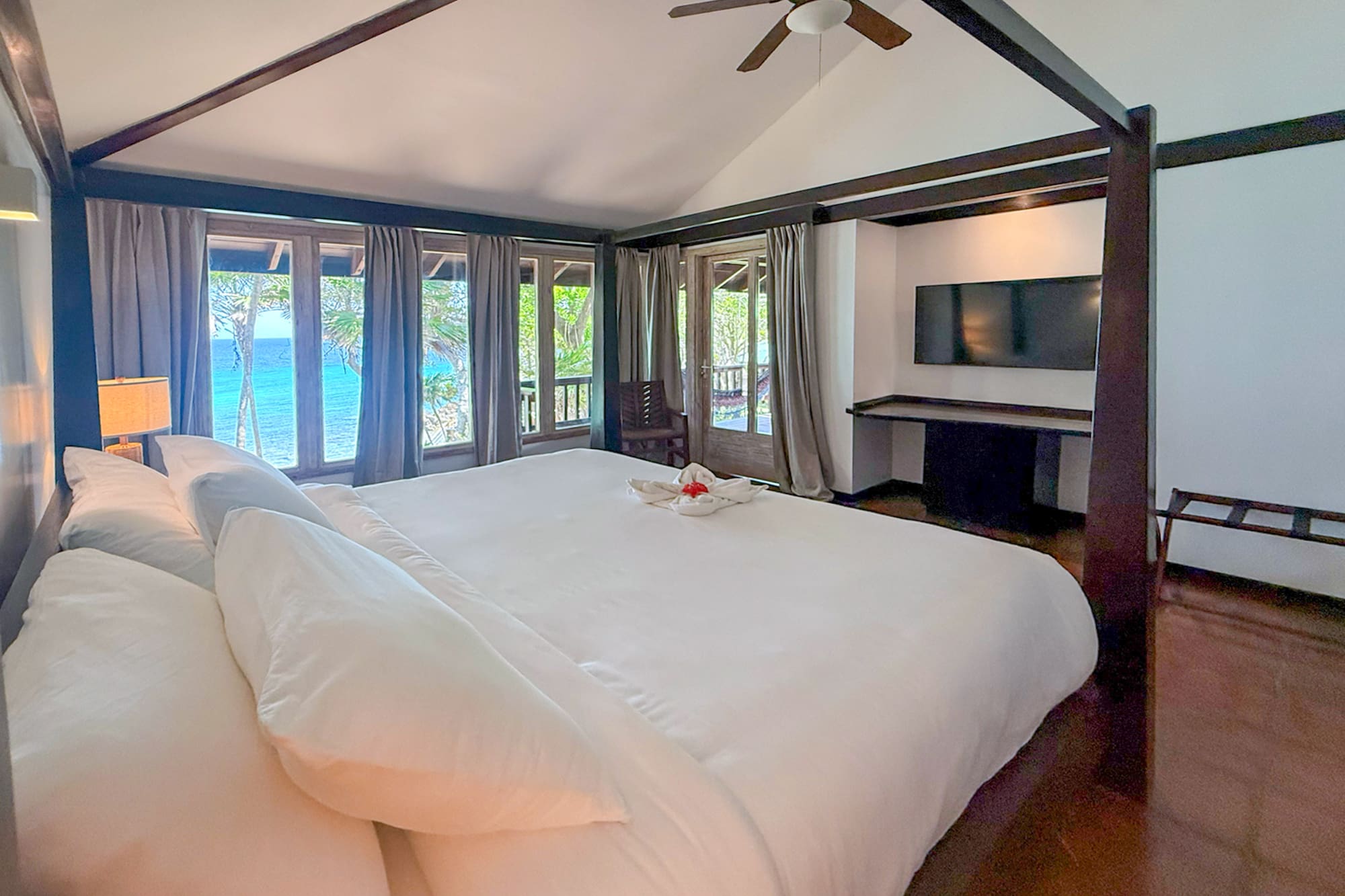 a large bed with white sheets and a television in a room with a view of the ocean
