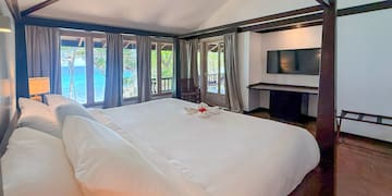 a large bed with white sheets and a television in a room with a view of the ocean