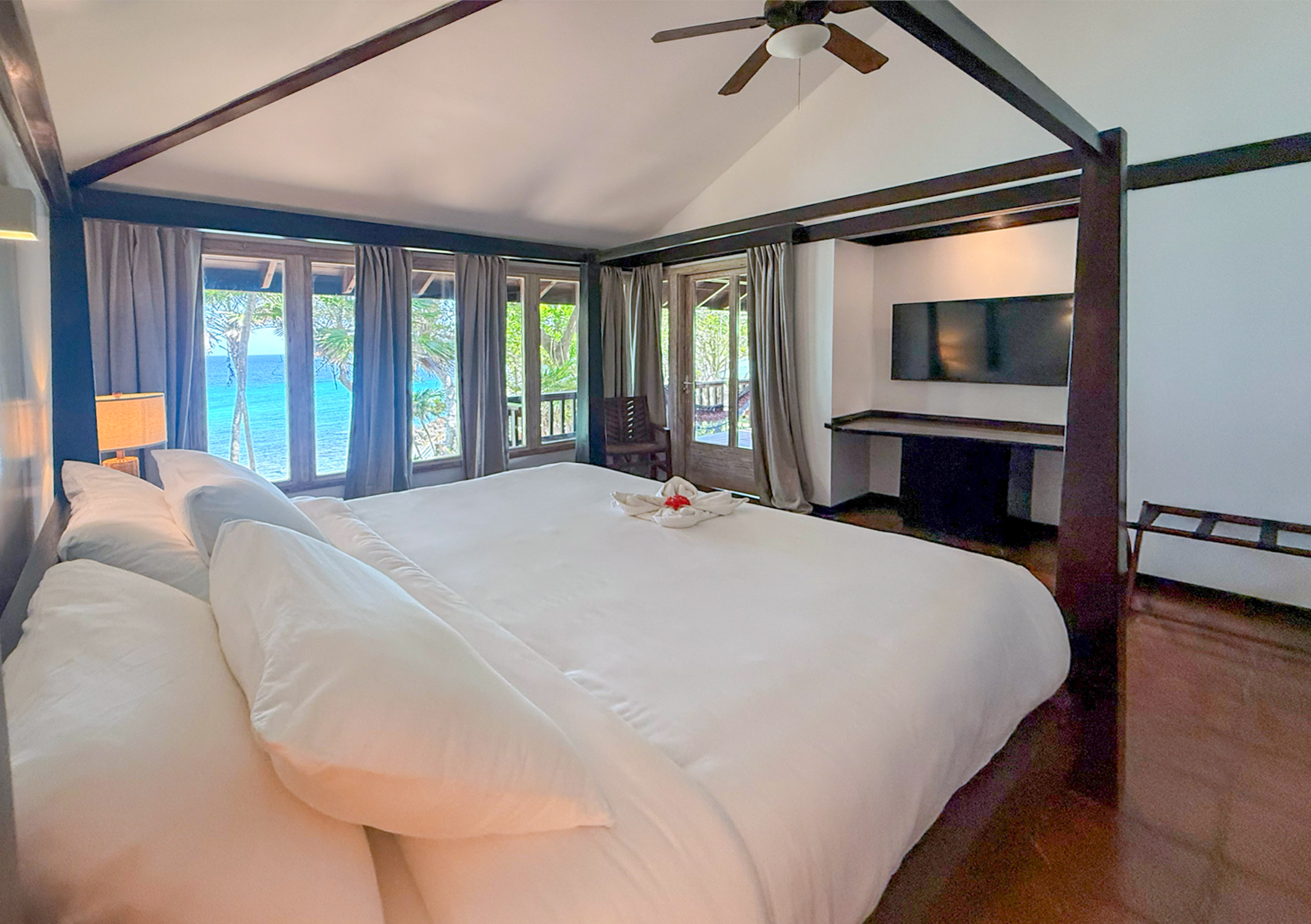 a large bed with white sheets and a television in a room with a view of the ocean