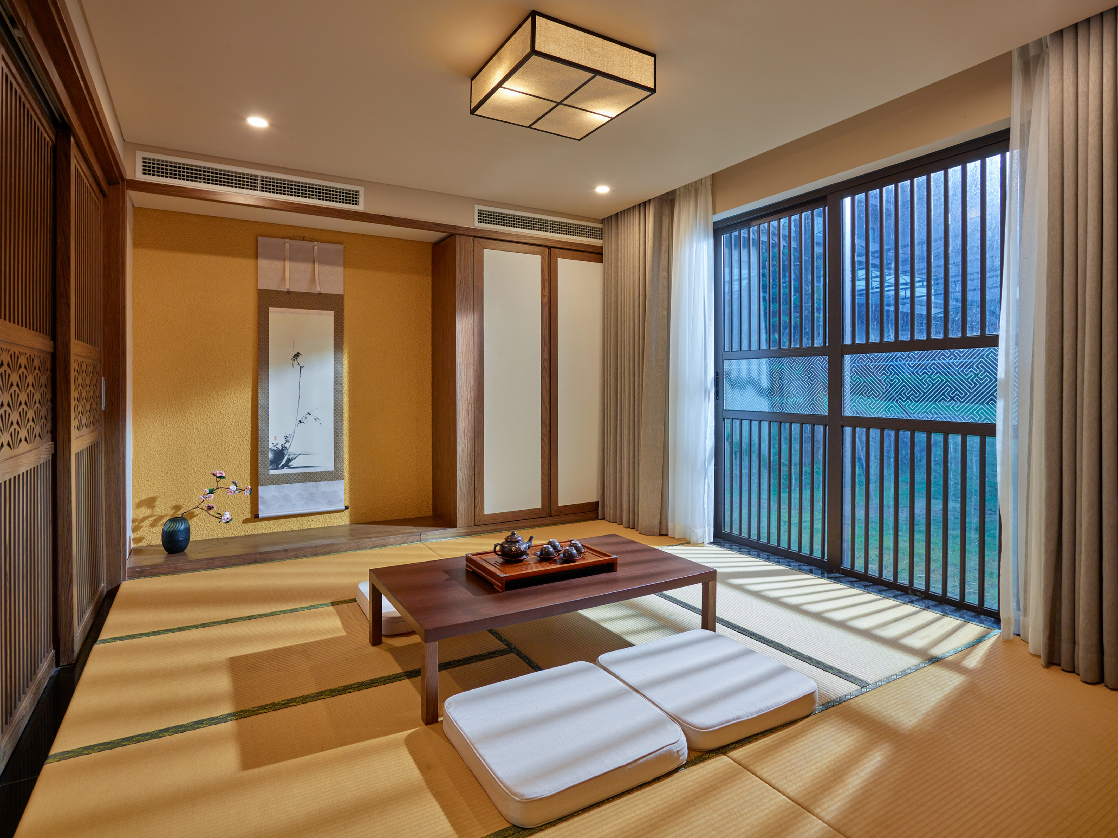 Japanese tatami room with low tea table, cushions, and sliding glass doors.