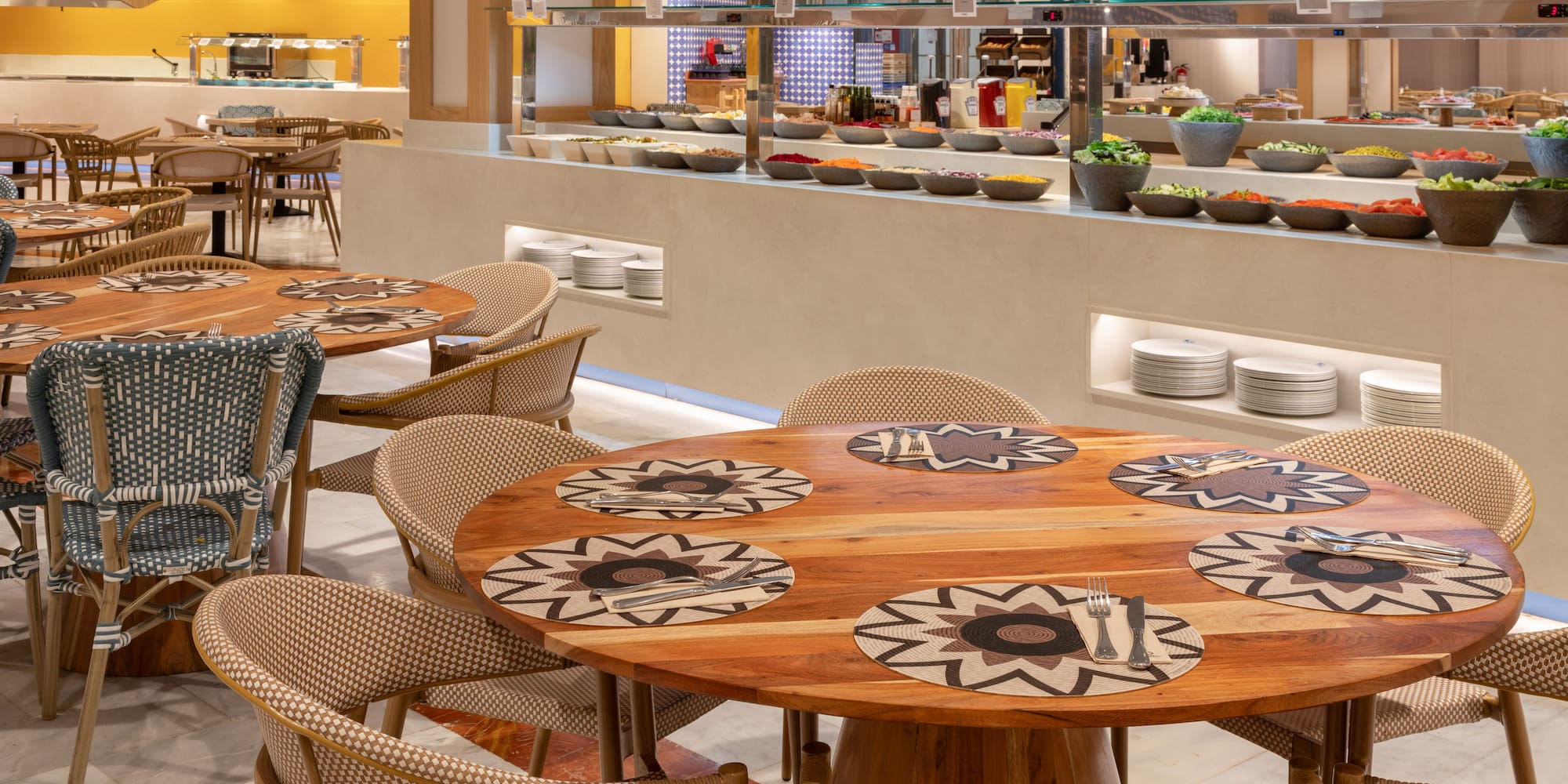 Buffet restaurant dining area with wooden tables, wicker chairs, and fresh salad bar.