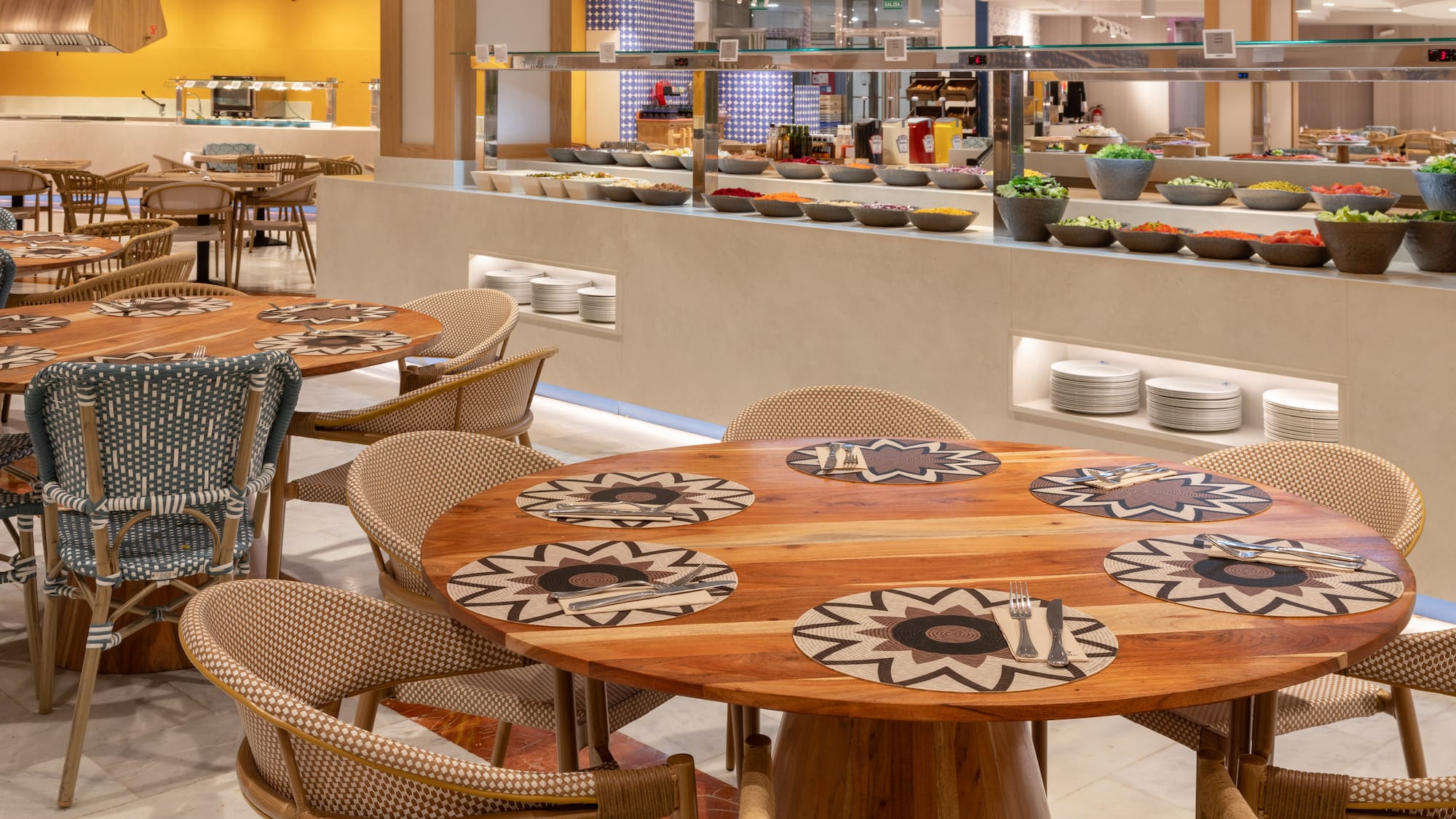 Buffet restaurant dining area with wooden tables, wicker chairs, and fresh salad bar.