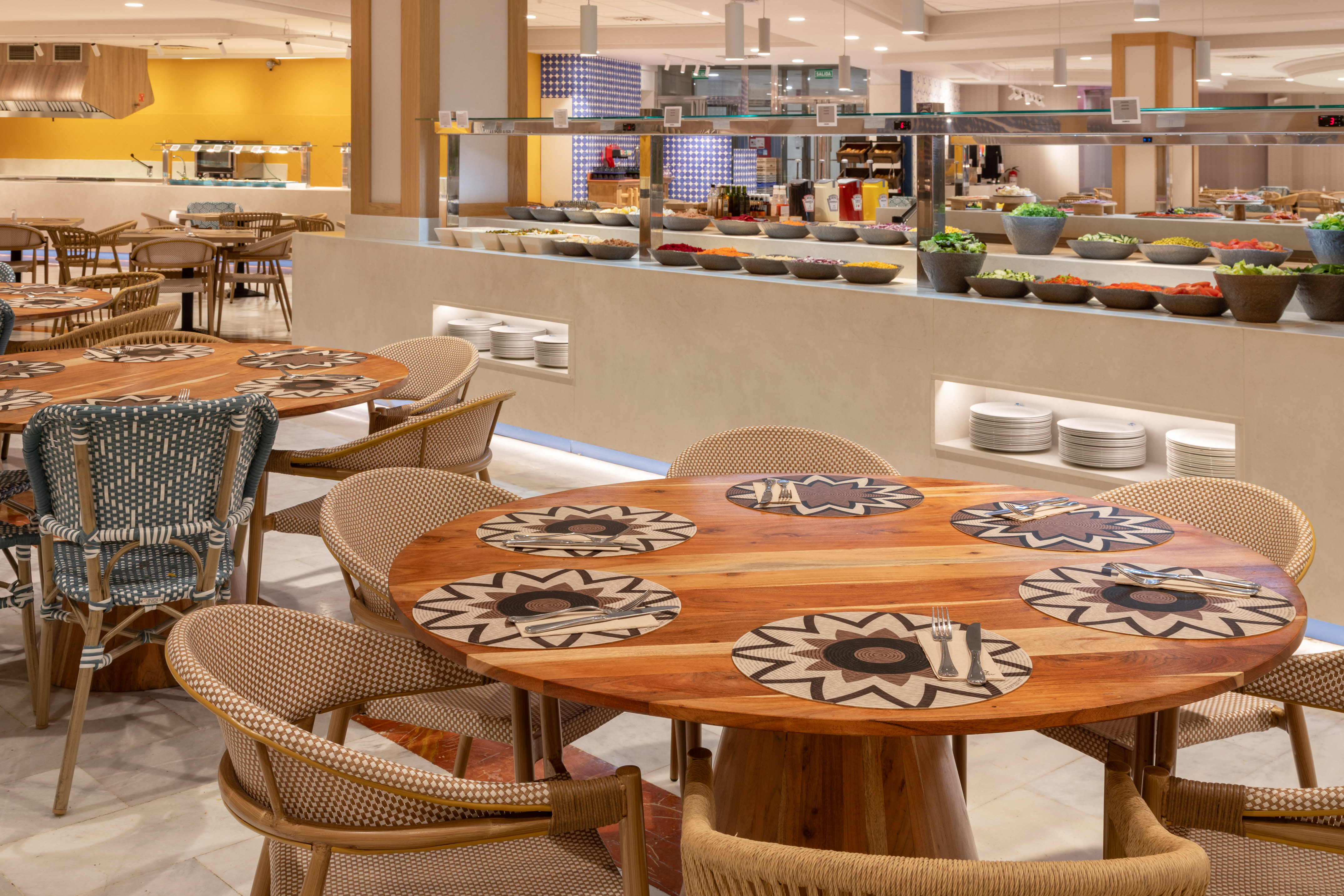 Buffet restaurant dining area with wooden tables, wicker chairs, and fresh salad bar.