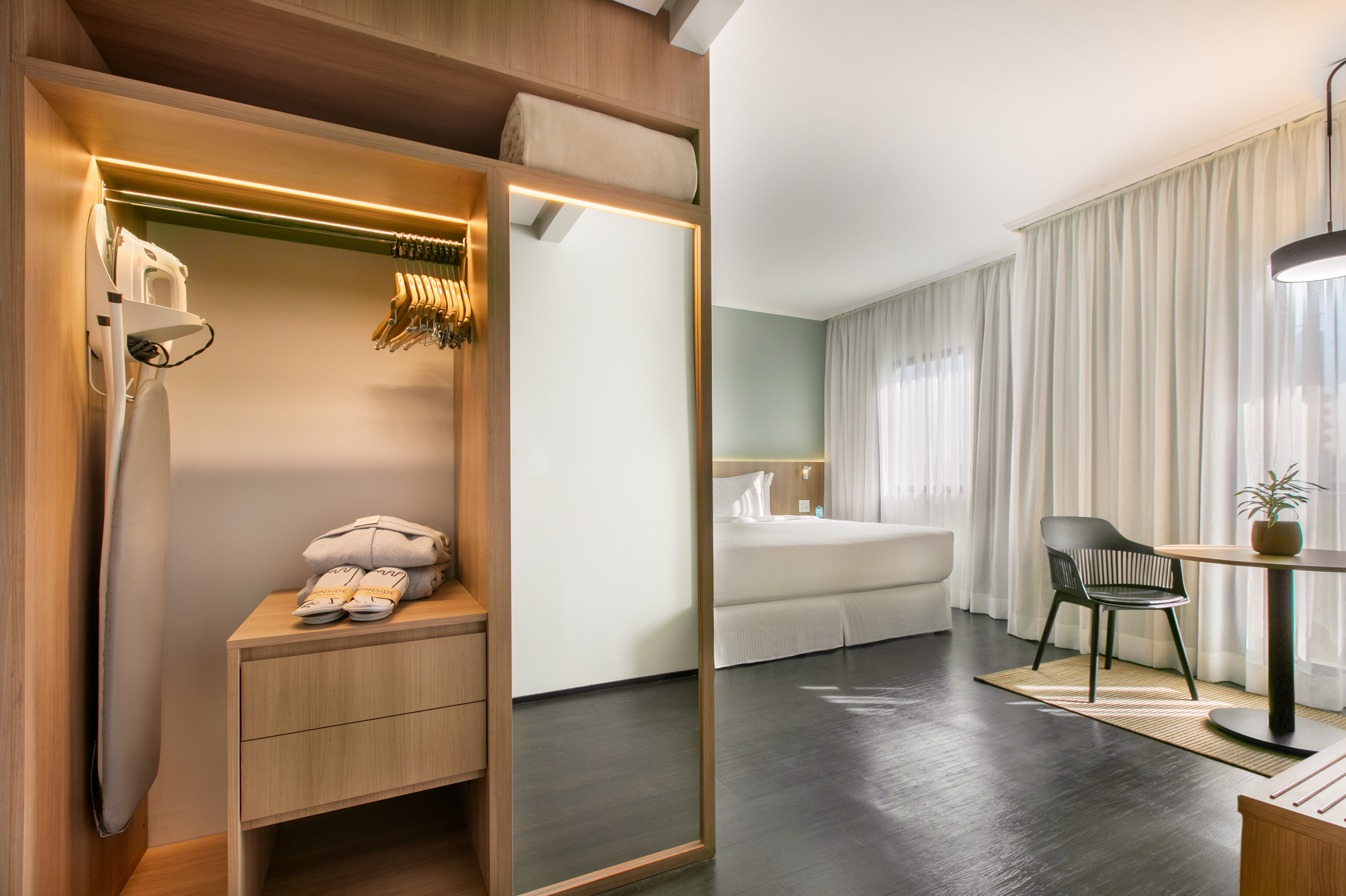 Hotel bedroom with modern wardrobe, iron, slippers, hangers, full mirror.