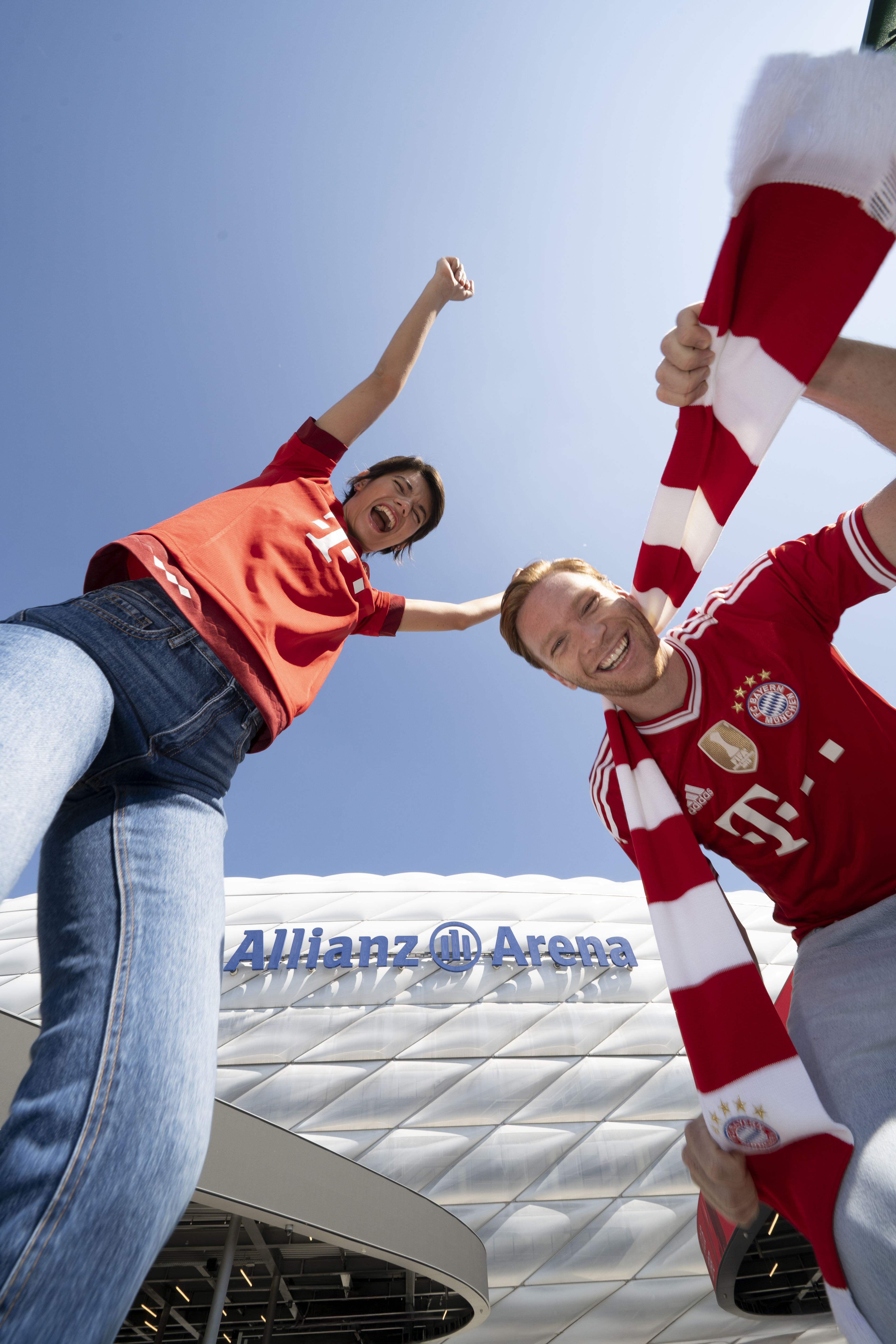 Cheering FC Bayern Munich fans in red jerseys outside Allianz Arena stadium.