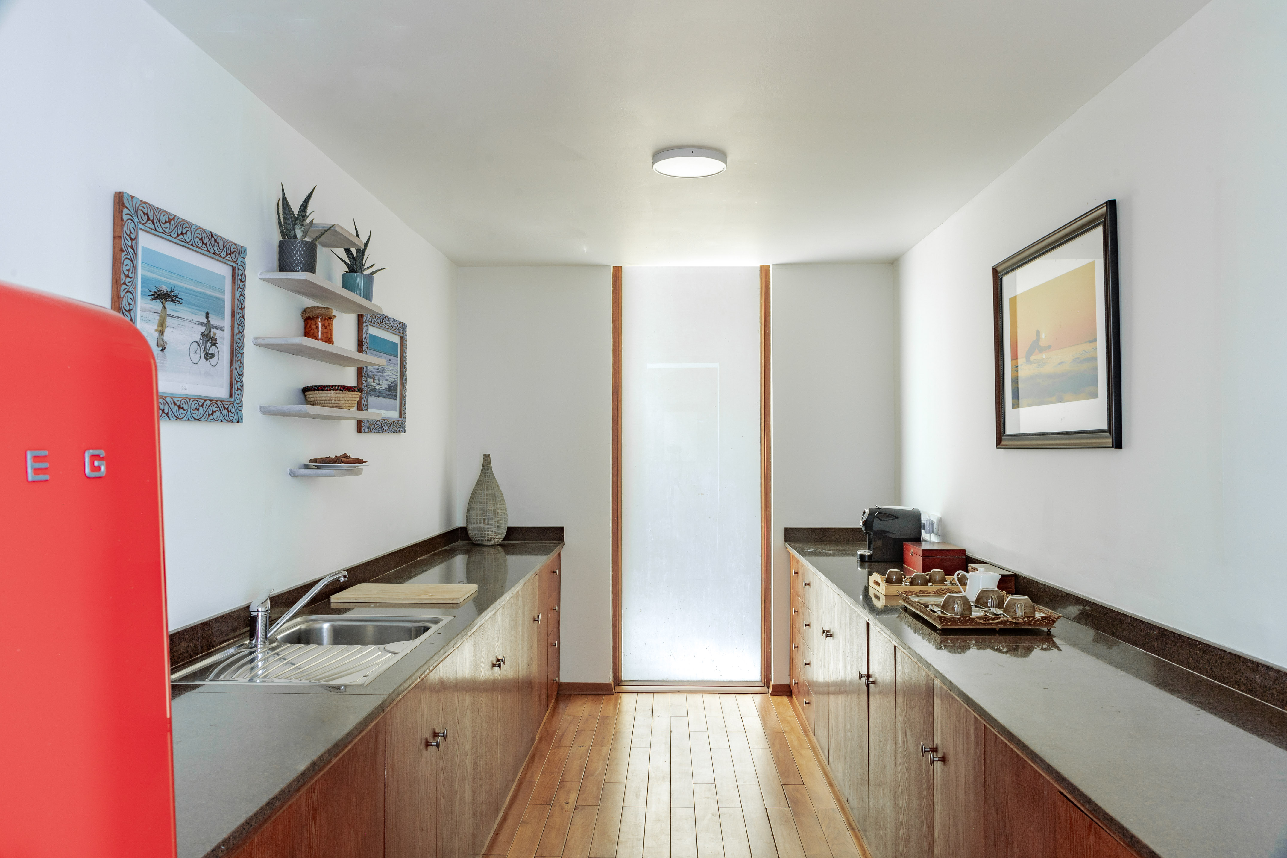 Compact modern kitchen with red Smeg fridge, dark counters, and wooden cabinetry.