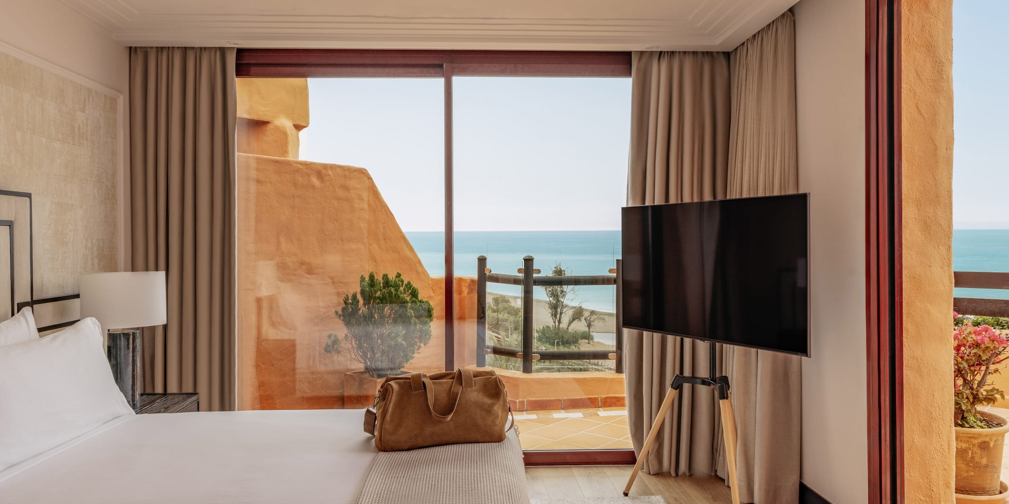 Beachfront hotel room featuring a bed, TV, and balcony with sea views.
