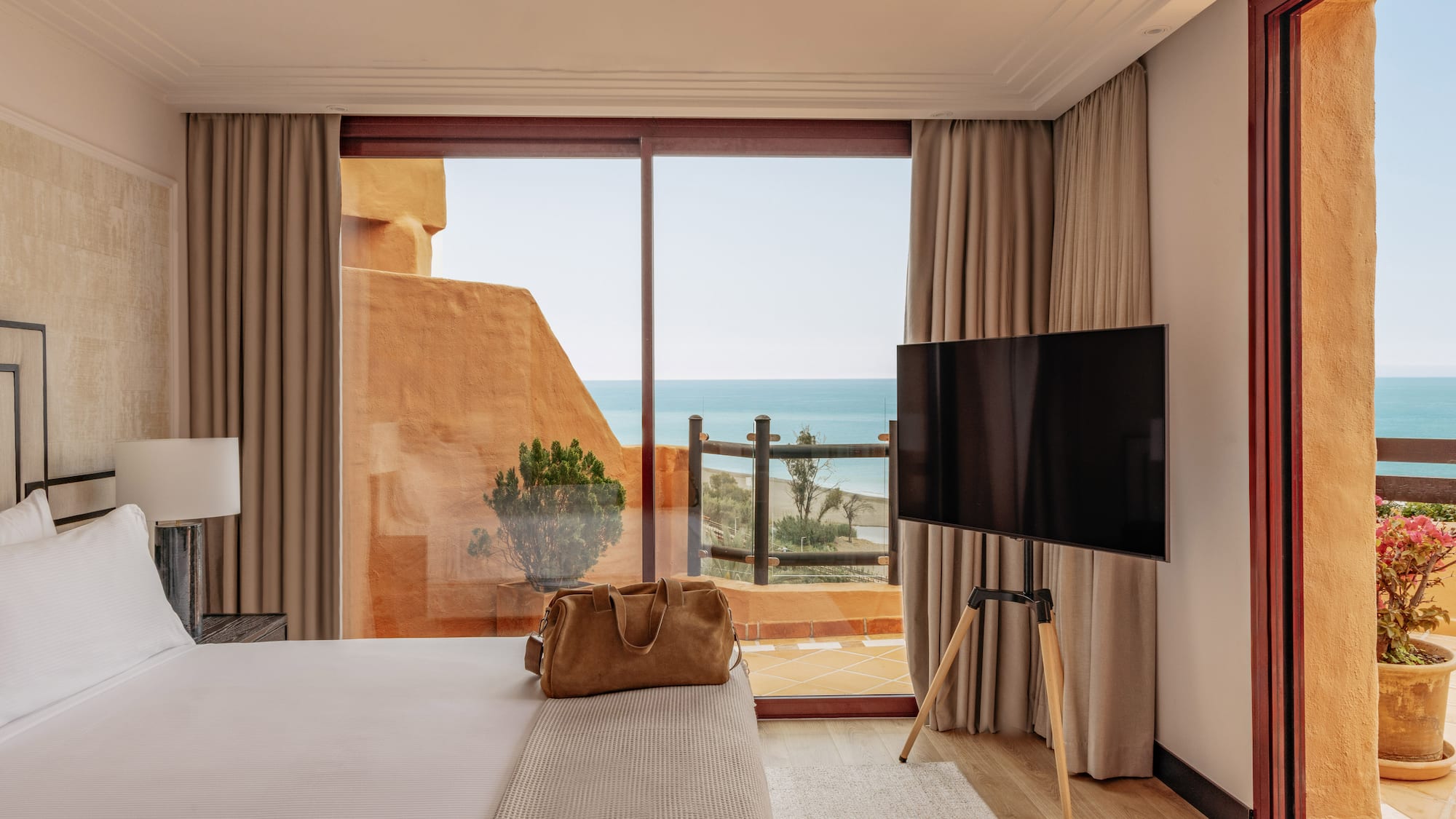 Beachfront hotel room featuring a bed, TV, and balcony with sea views.