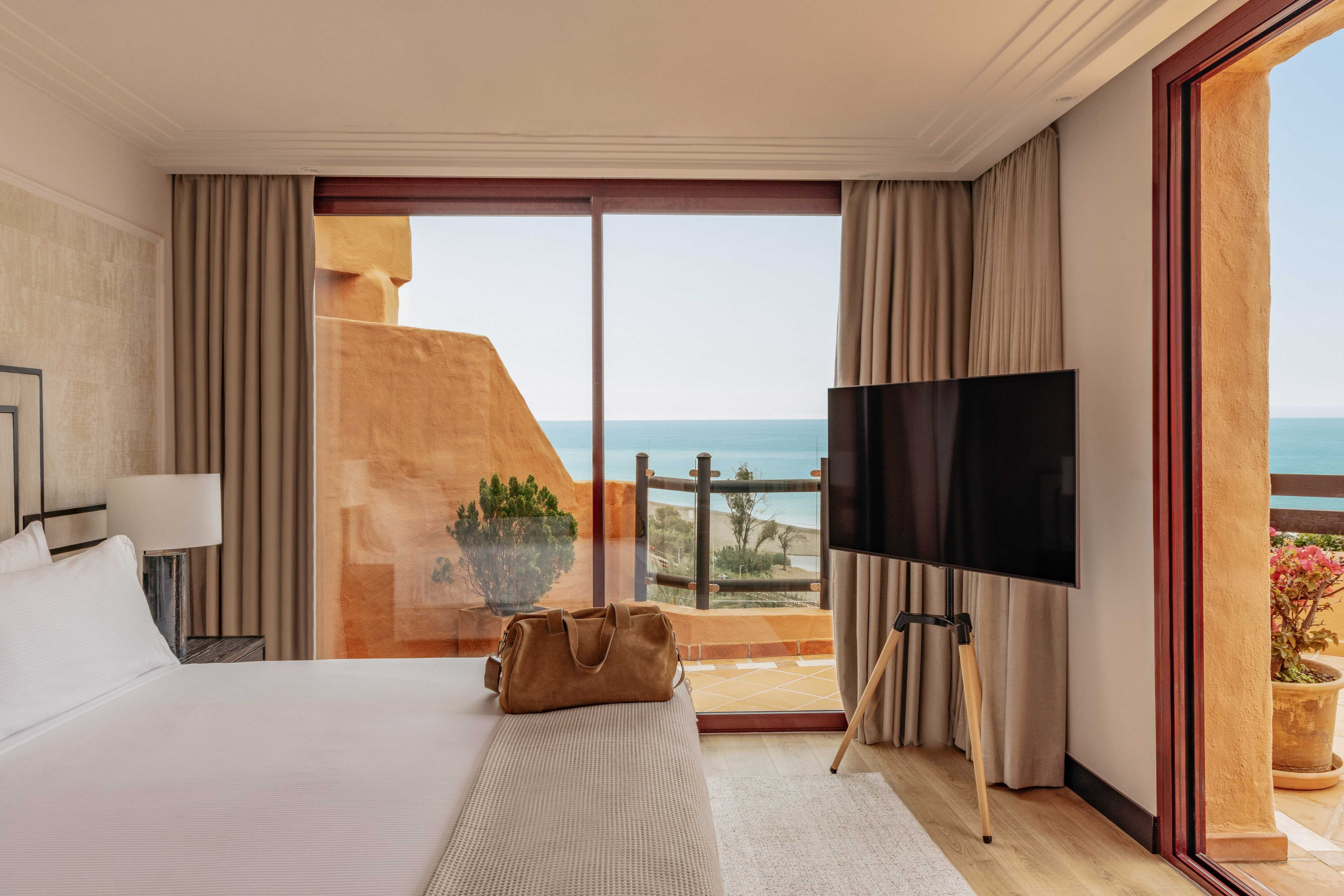 Beachfront hotel room featuring a bed, TV, and balcony with sea views.