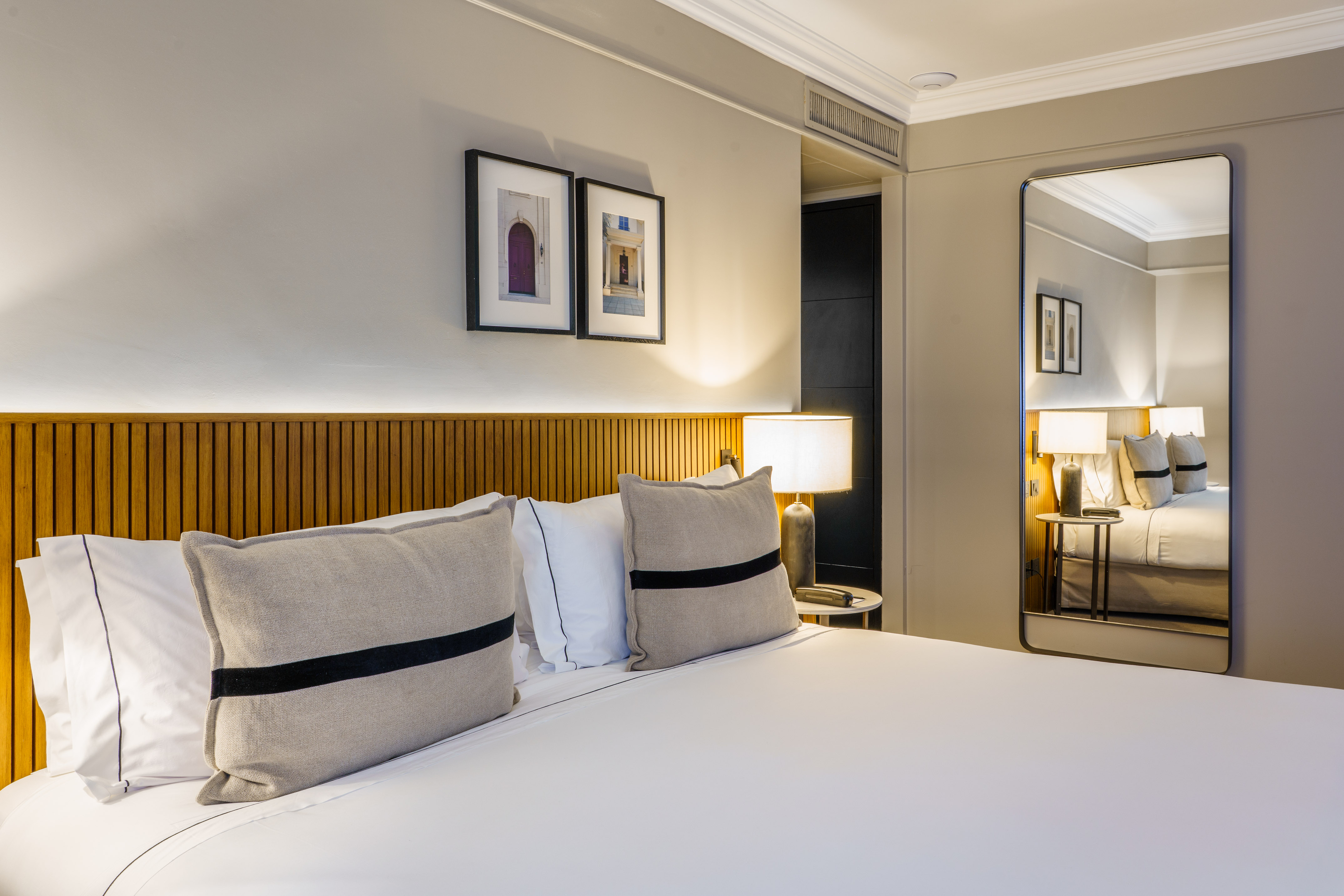 Modern hotel room with white bed, wooden headboard, lamps, and large mirror.