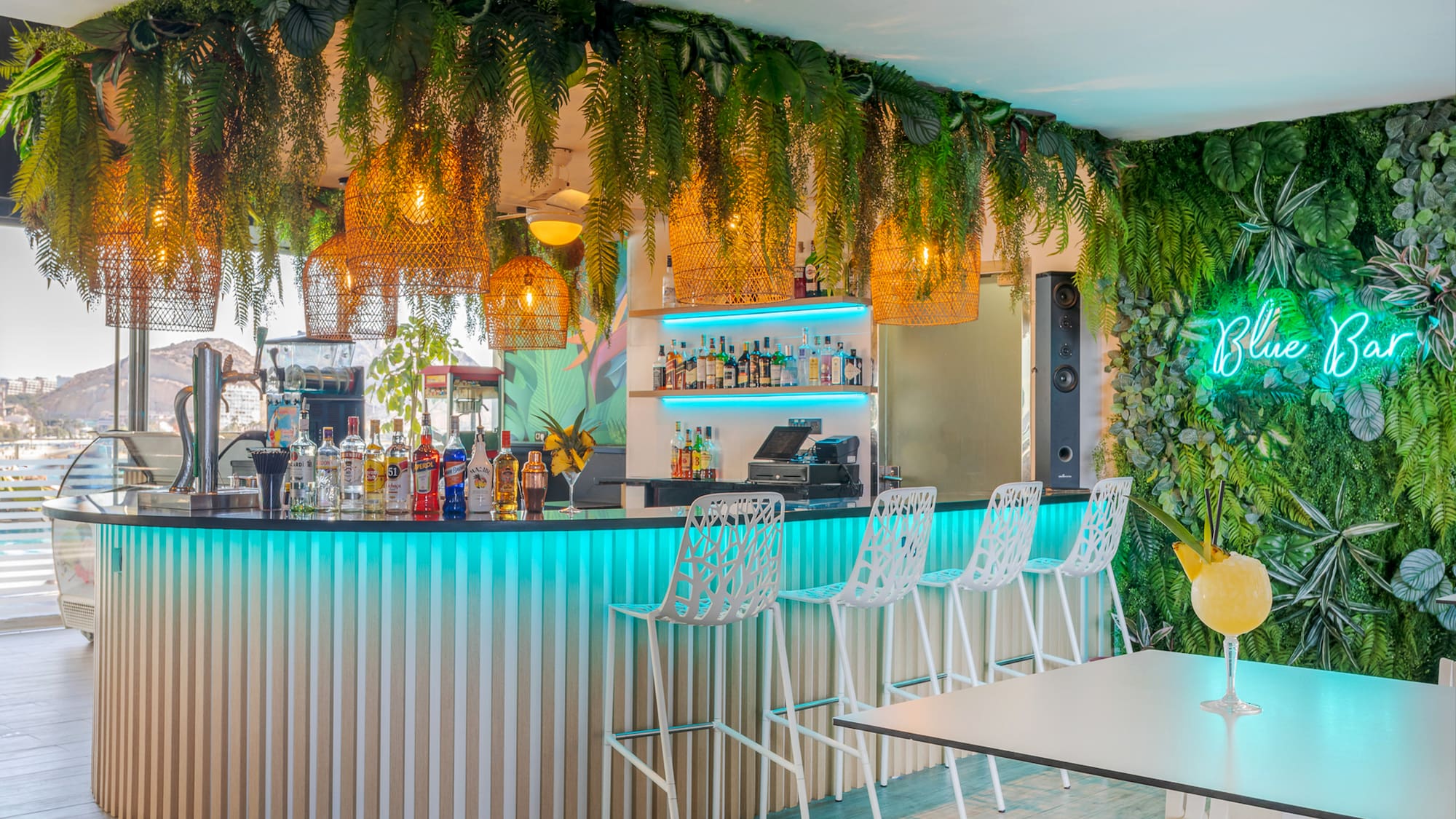a bar with white chairs and a table with plants from the ceiling
