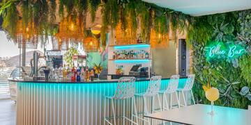 a bar with white chairs and a table with plants from the ceiling