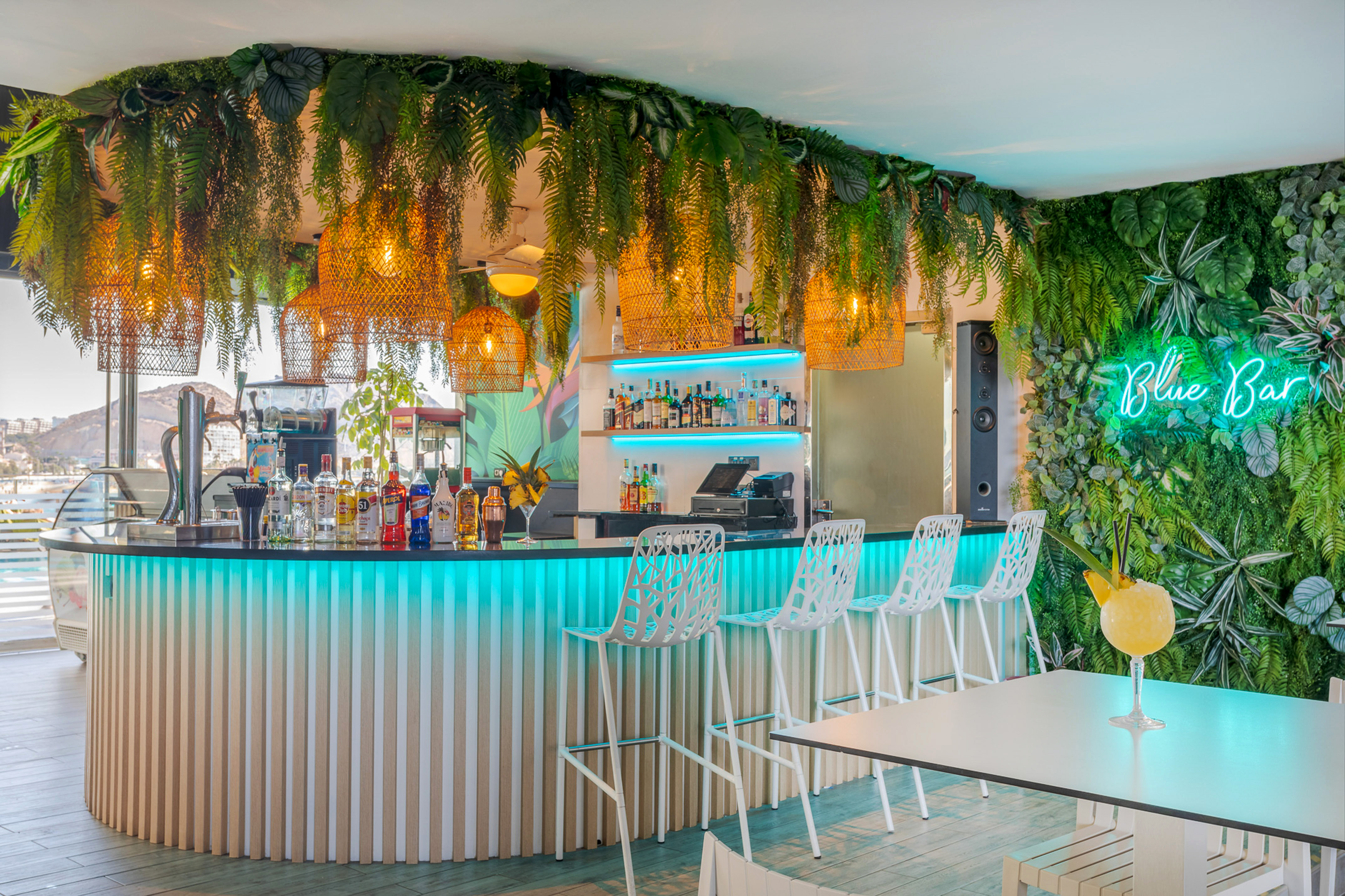 Modern tropical cocktail bar with Blue Bar neon sign and lush green decor.