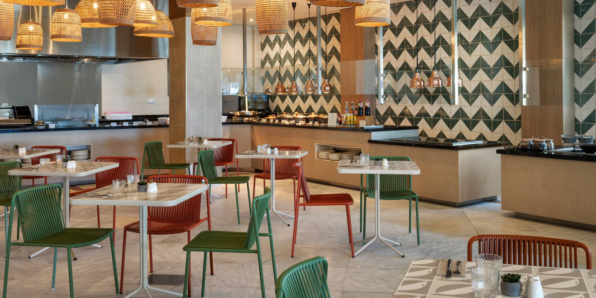 Modern restaurant buffet with green and orange chairs, wicker lamps, tiled walls.