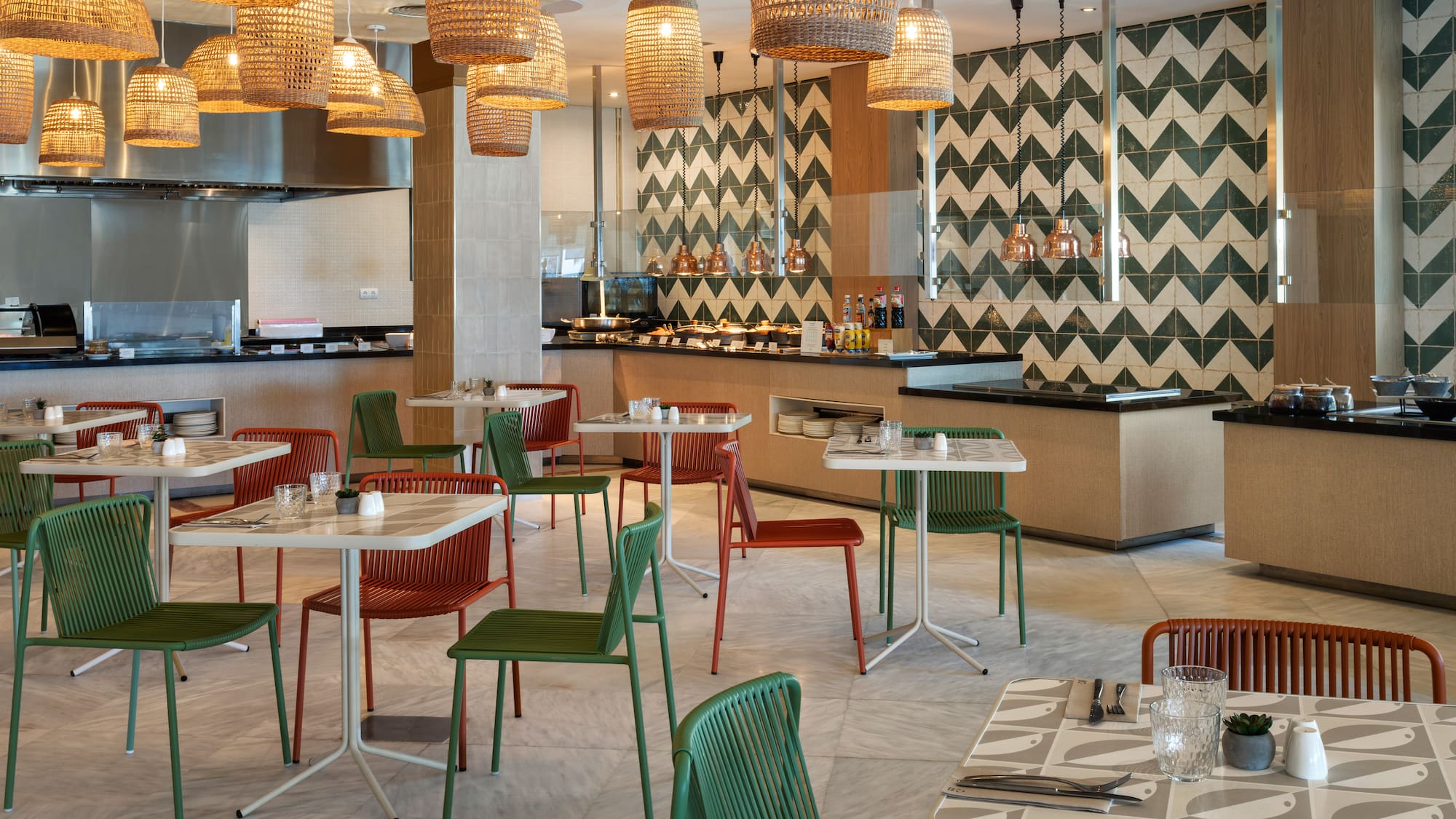 Modern restaurant buffet with green and orange chairs, wicker lamps, tiled walls.