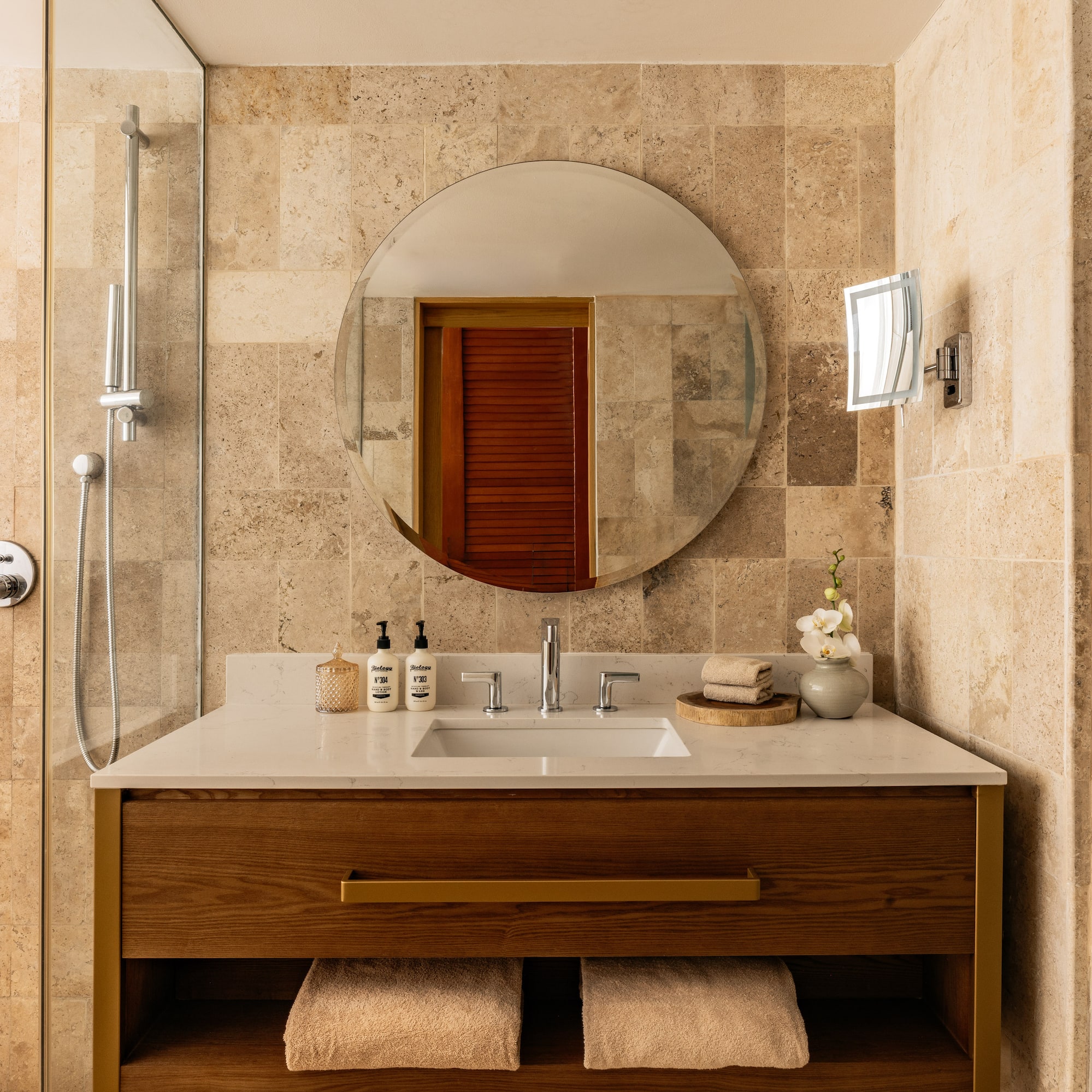 Modern bathroom with wood vanity, round mirror, white counter, and tiled shower.