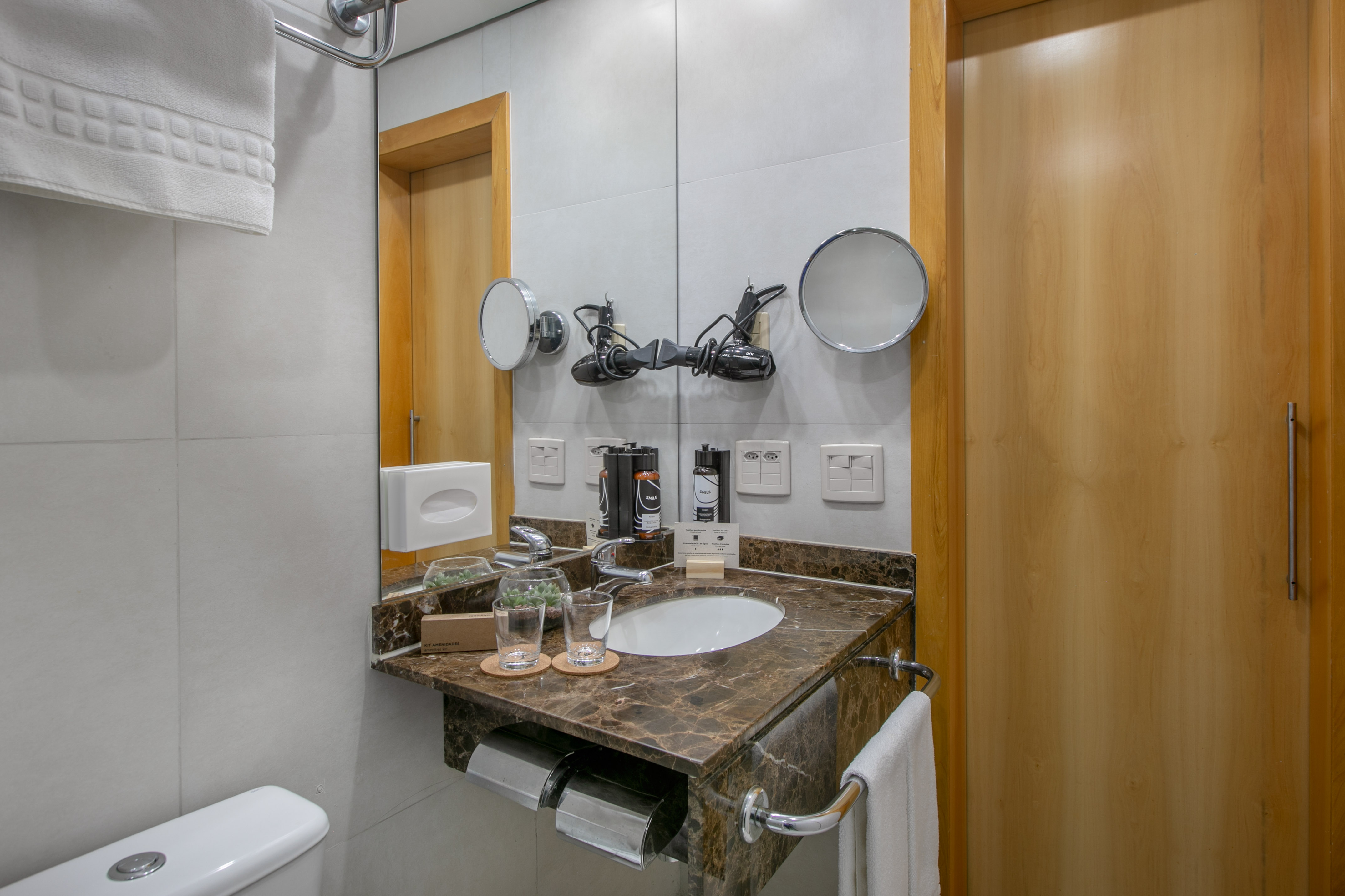 Modern hotel bathroom with marble vanity, sink, mirror, toiletries, and hair dryers.