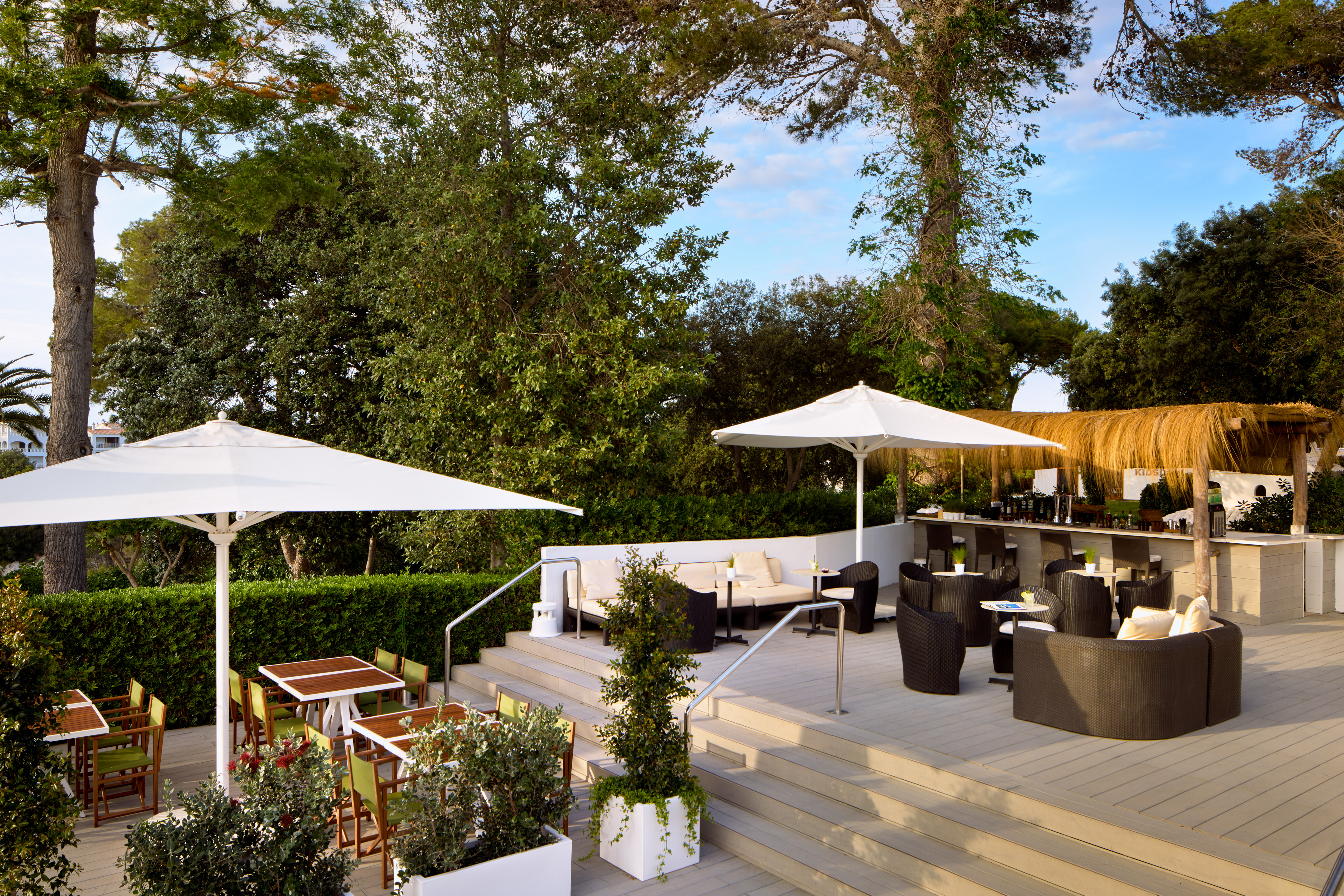 Lush outdoor patio bar and restaurant seating under white umbrellas.
