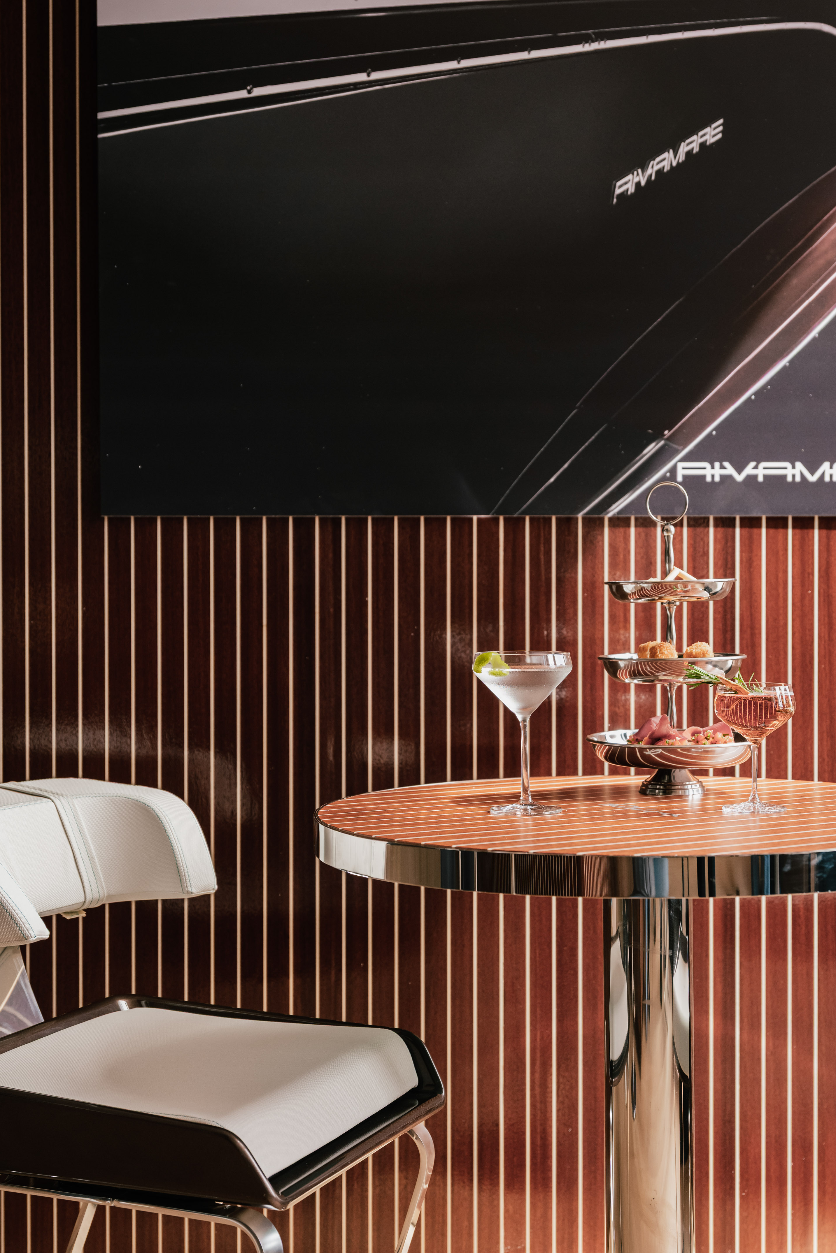 Rivamare bar: cocktails, tiered appetizers, wooden table, and sleek white chair.