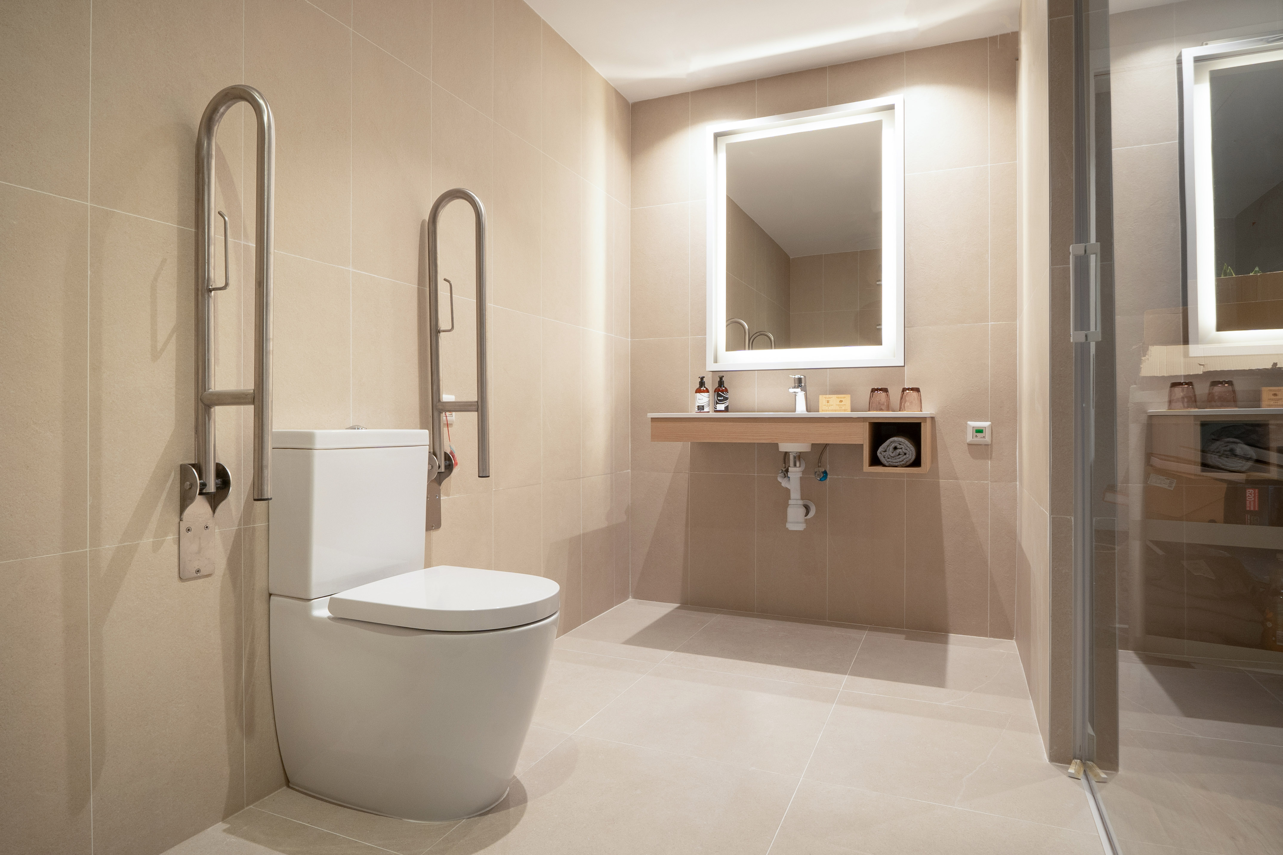 Accessible bathroom with toilet, grab bars, modern vanity, and neutral tiles.