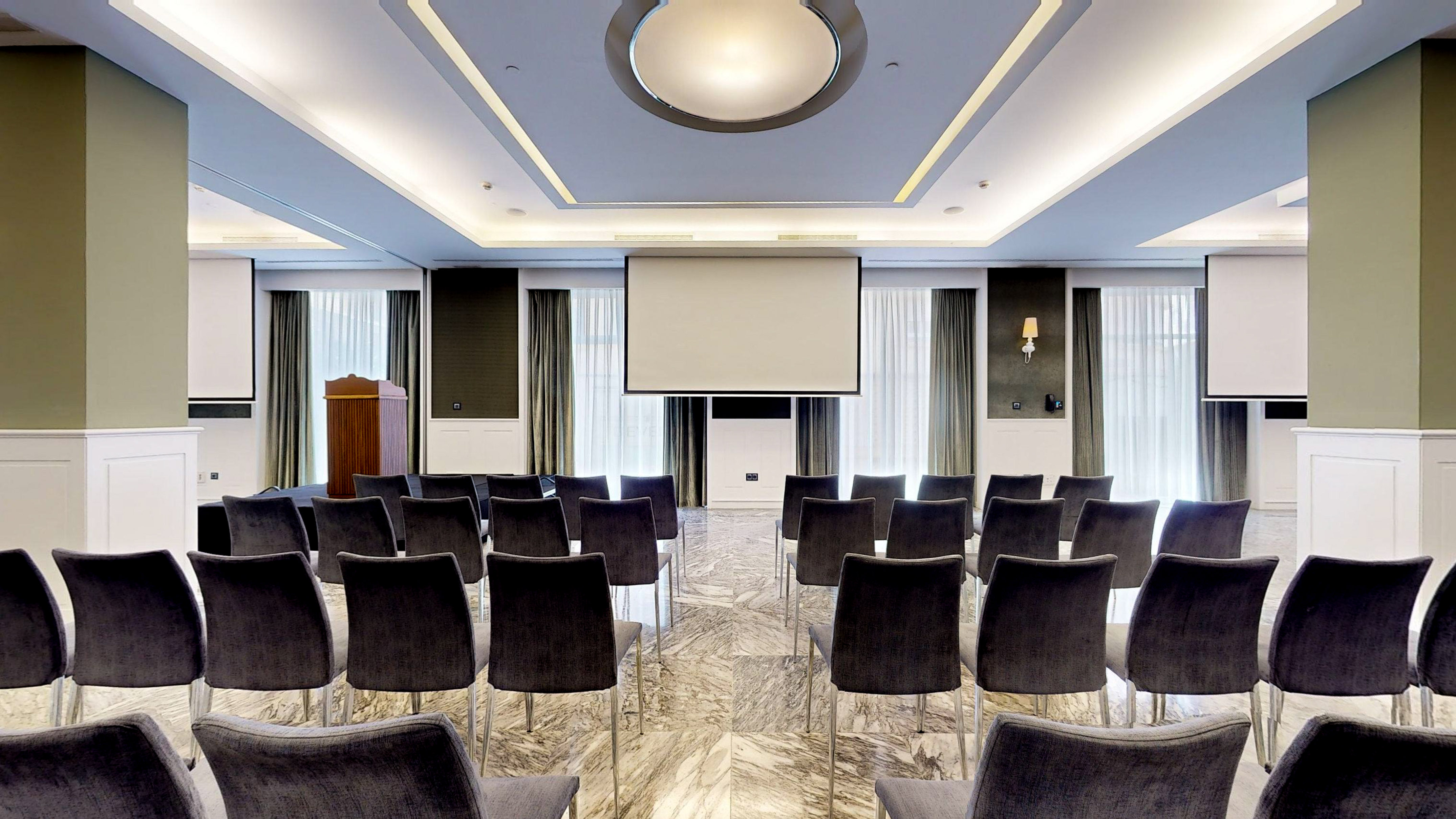 Modern conference room with dark chairs, large projection screen, and wooden lectern.