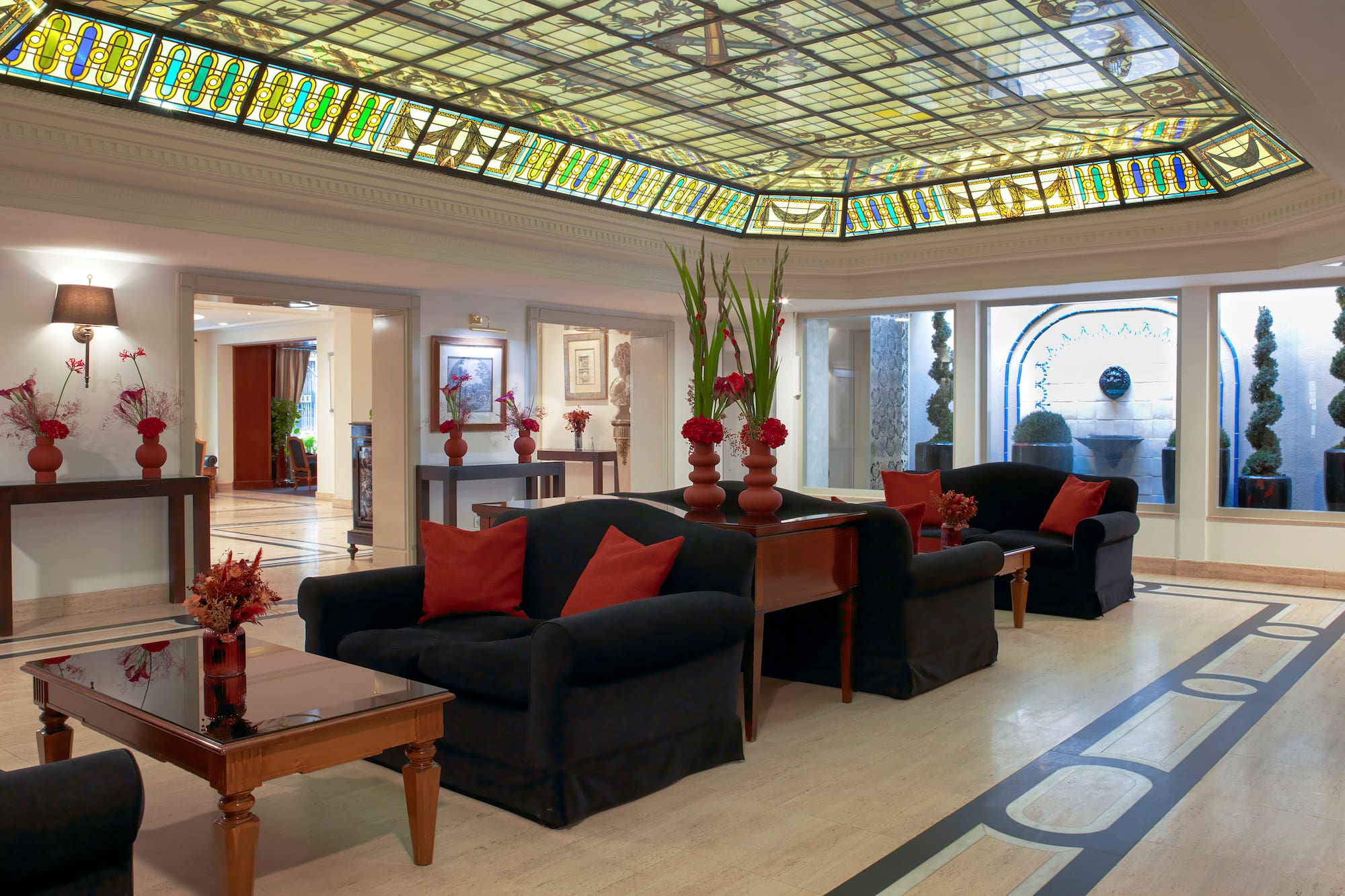 Elegant hotel lobby with stained glass ceiling, black sofas, and red floral decor.