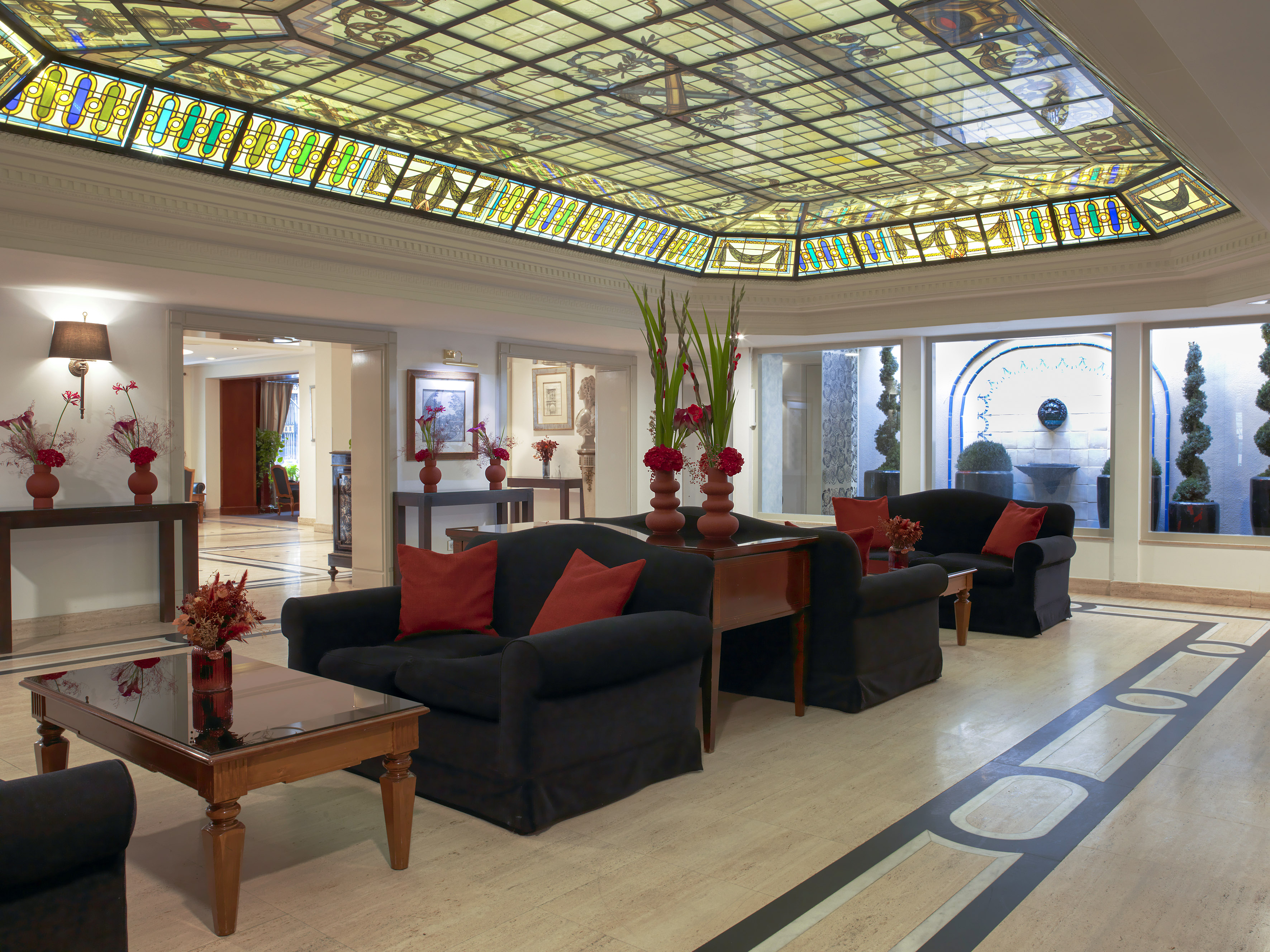 Elegant hotel lobby with stained glass ceiling, black sofas, and red floral decor.