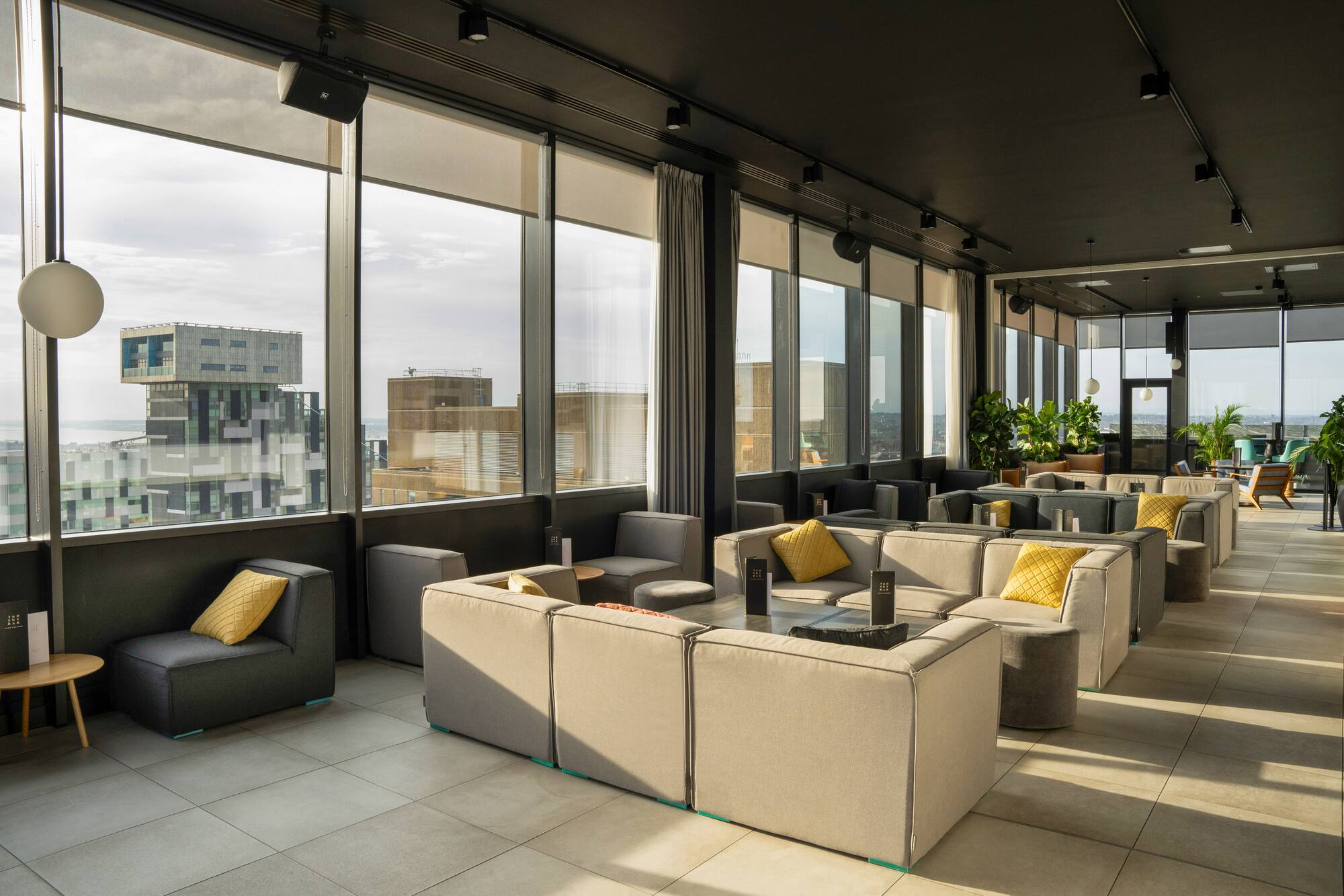 Modern rooftop lounge with modular sofas, city views, and yellow cushions.
