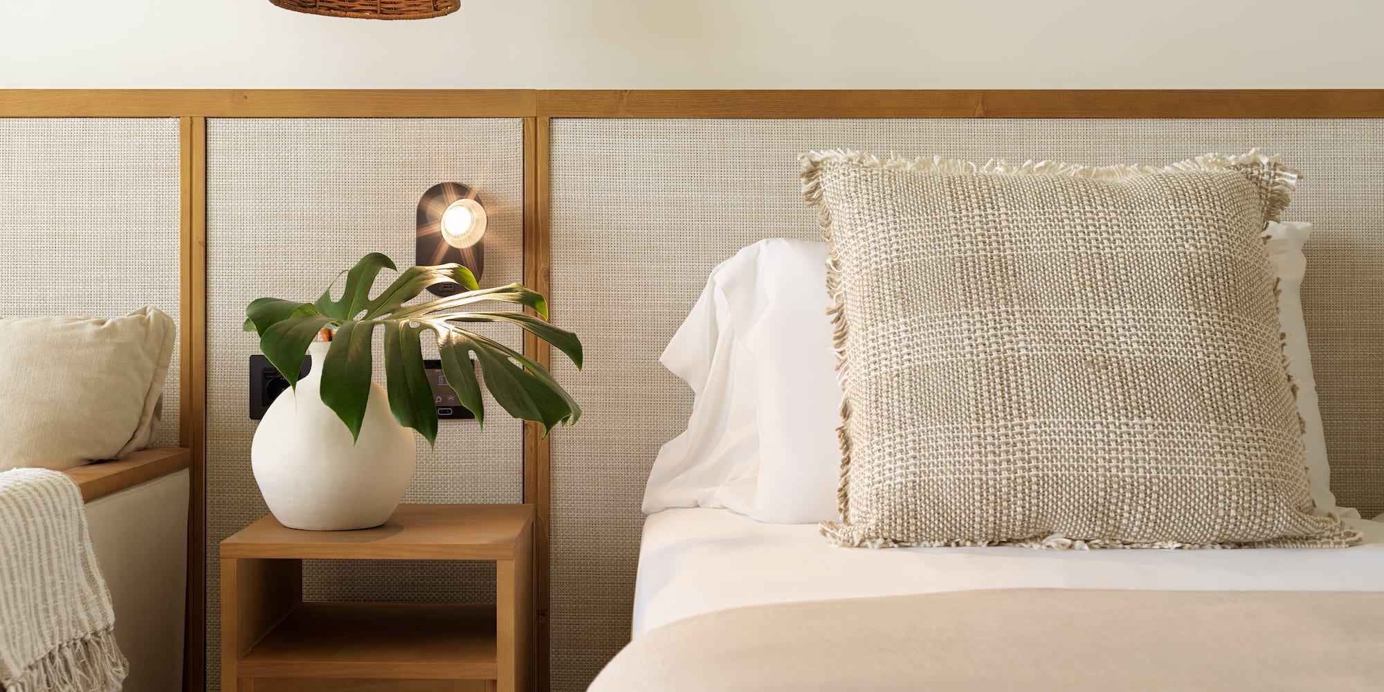 Bedroom with cane headboard, wood nightstand, plant, and neutral bedding.