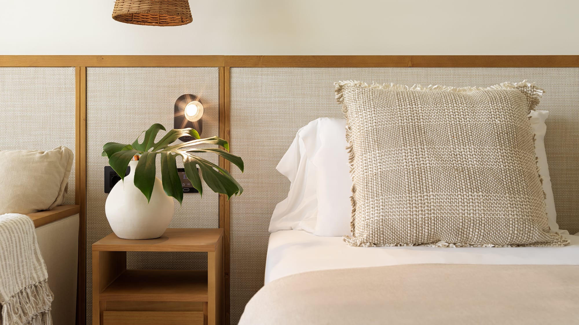Bedroom with cane headboard, wood nightstand, plant, and neutral bedding.