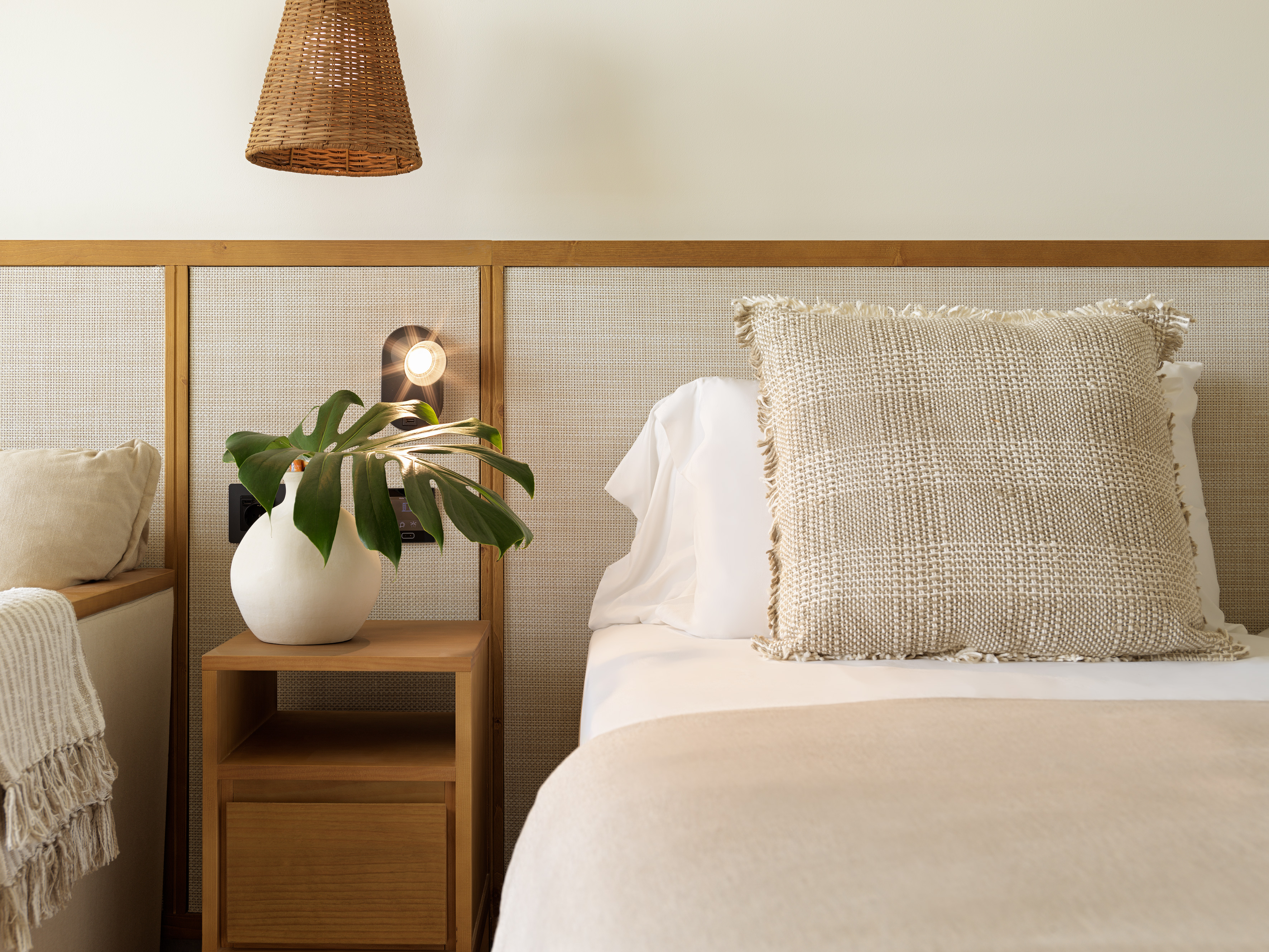 Bedroom with cane headboard, wood nightstand, plant, and neutral bedding.