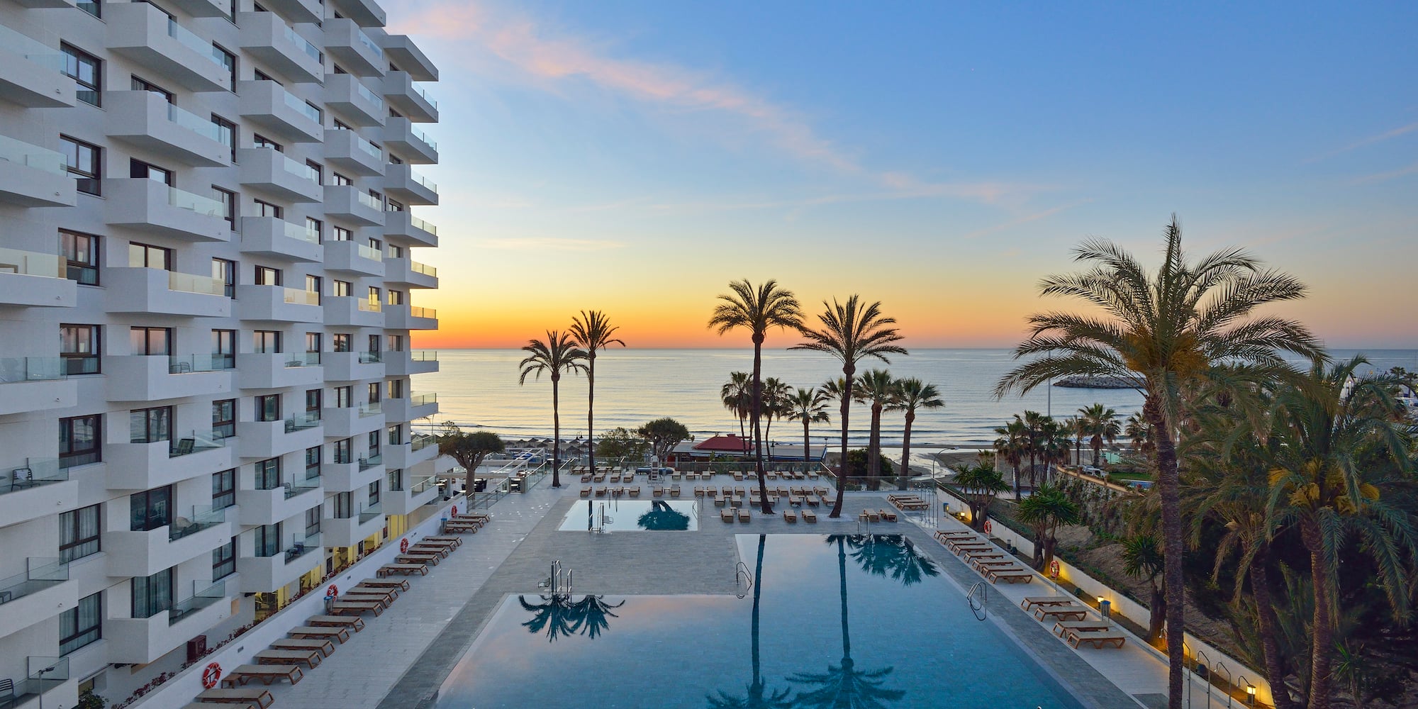 a pool with palm trees and a building with a beach in the background