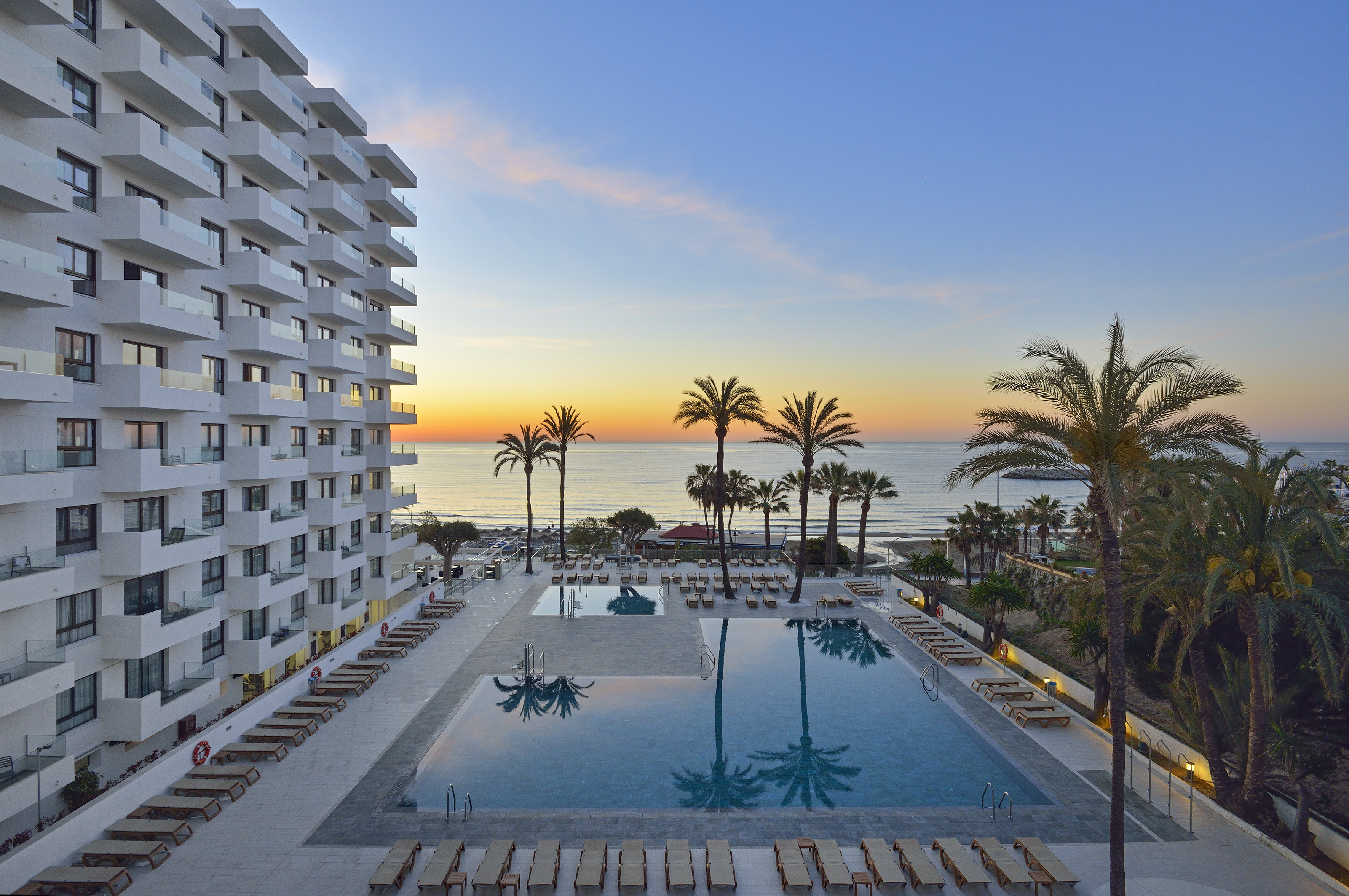 a pool with palm trees and a building with a beach in the background