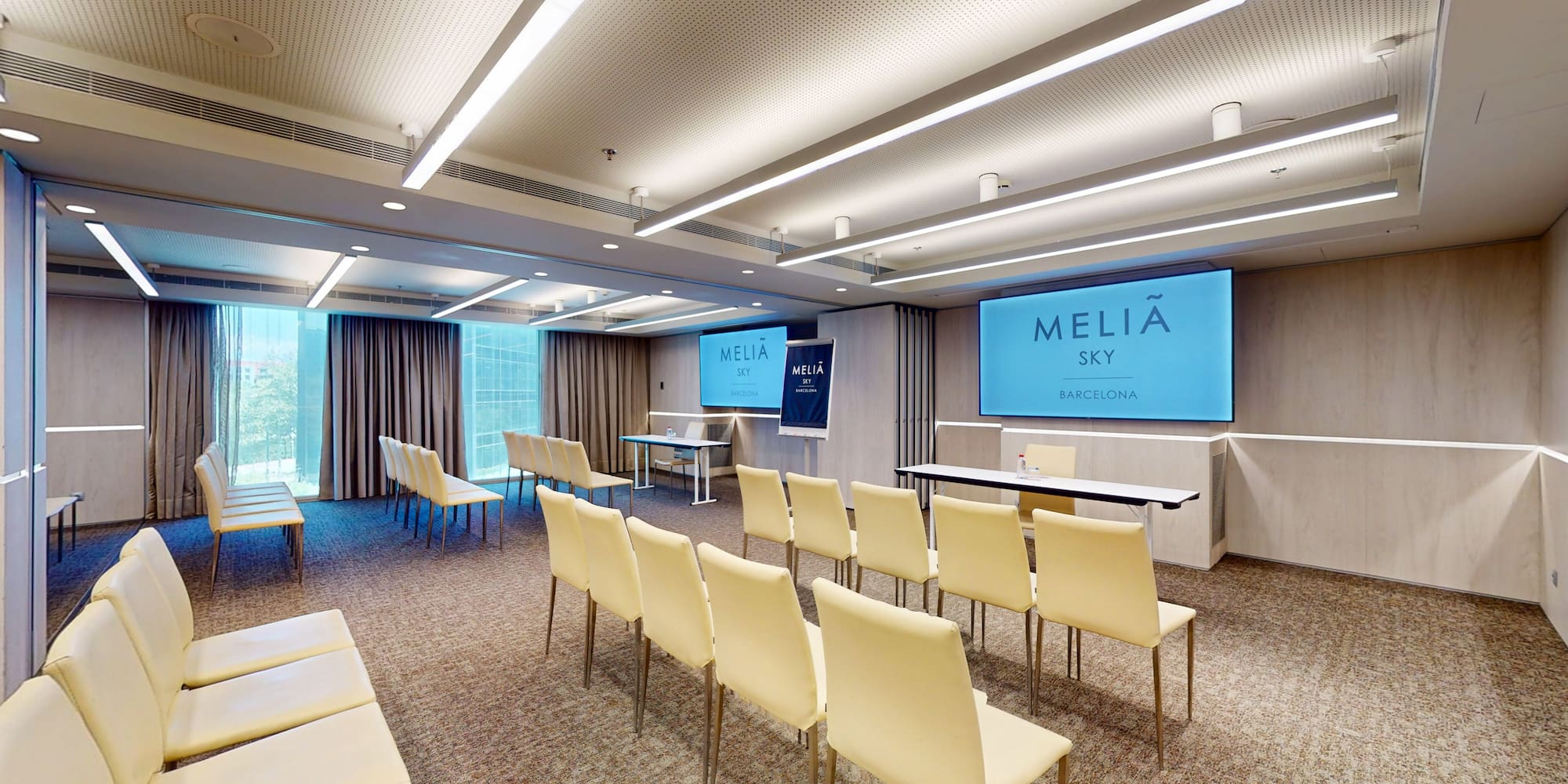 Melia Sky Barcelona modern conference room with light chairs and dual screens.