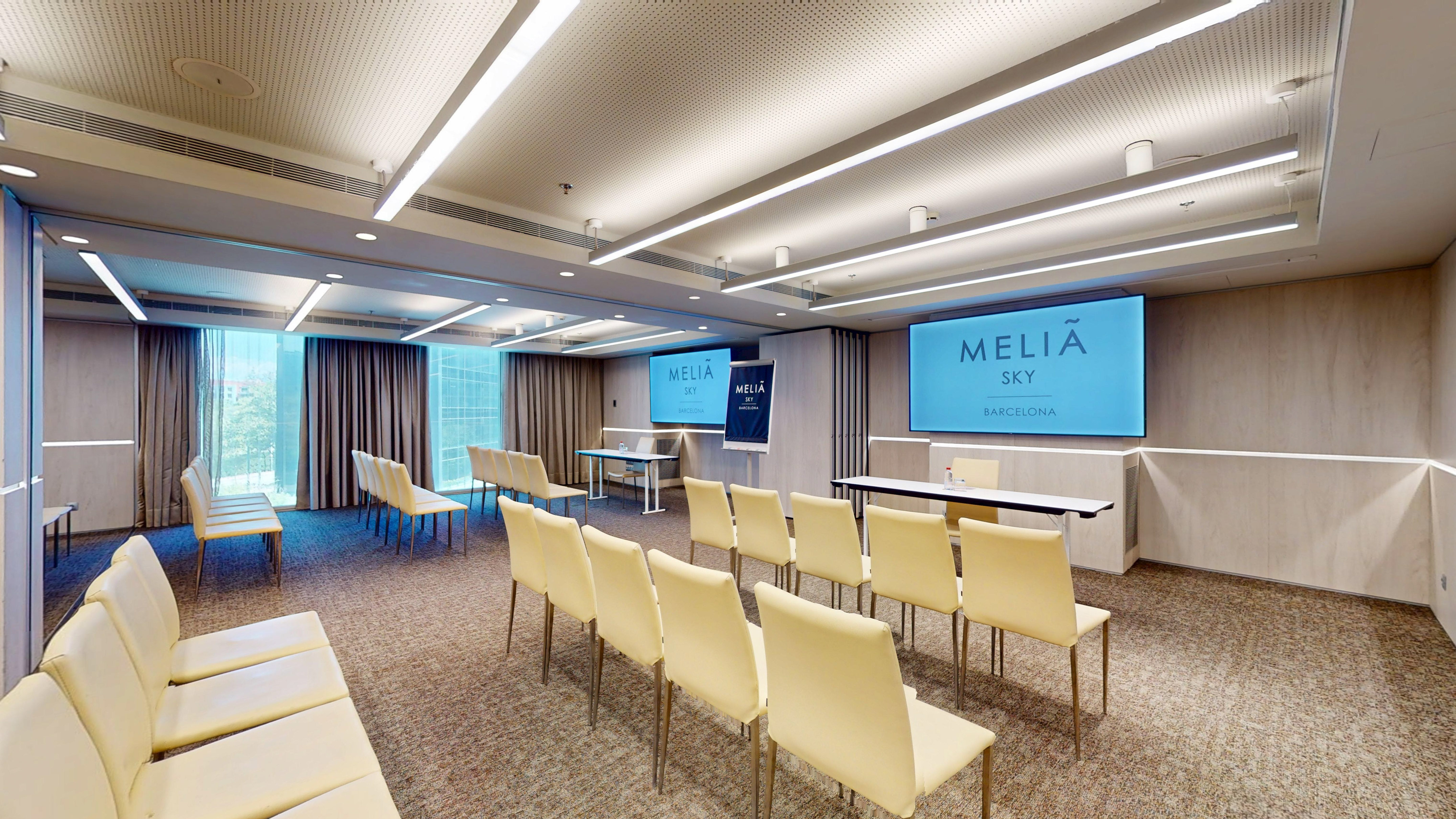 Melia Sky Barcelona modern conference room with light chairs and dual screens.