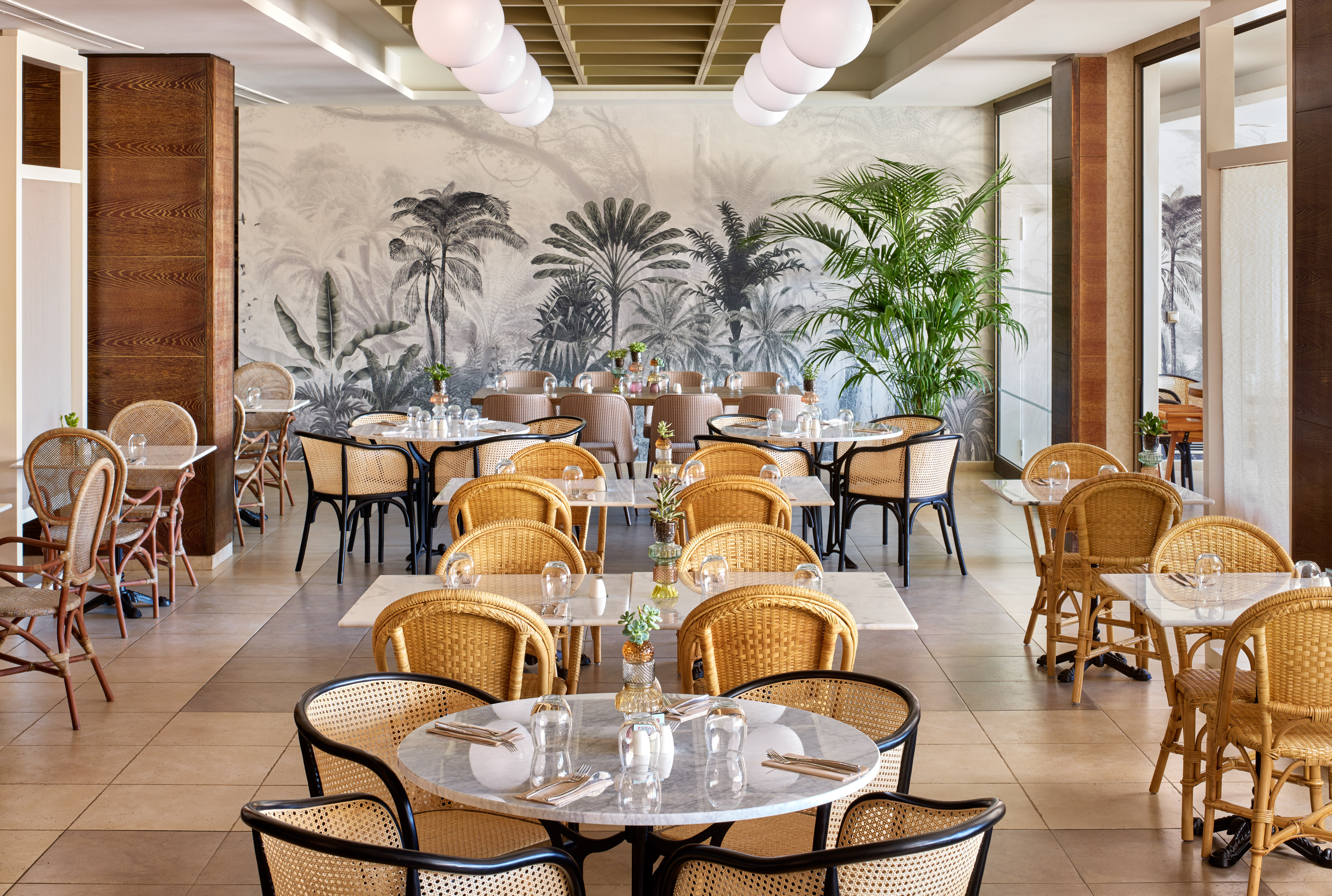 Restaurant dining room with tropical wallpaper, rattan chairs, and marble tables.