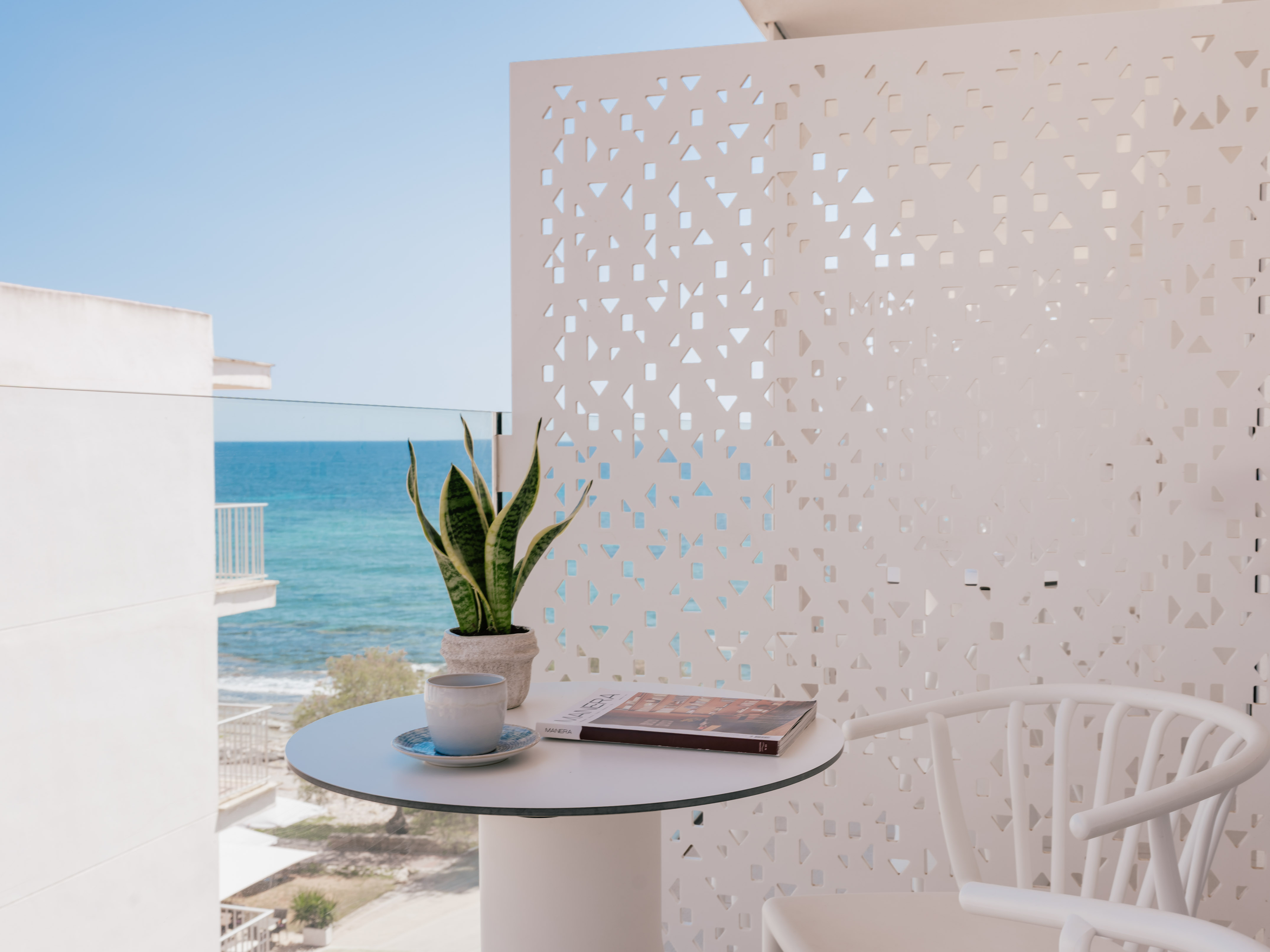 Balcón moderno con vista al mar. Mesa, café, planta, panel decorativo.