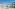Sunny beach resort with white hotel buildings, palm trees, lounge chairs.