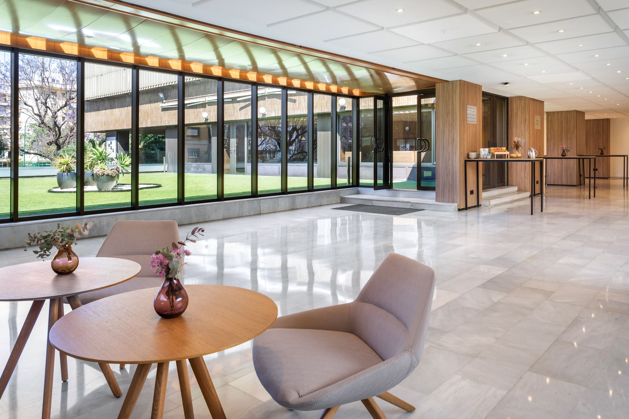Modern hotel lobby lounge with bright marble floor and lush garden views.
