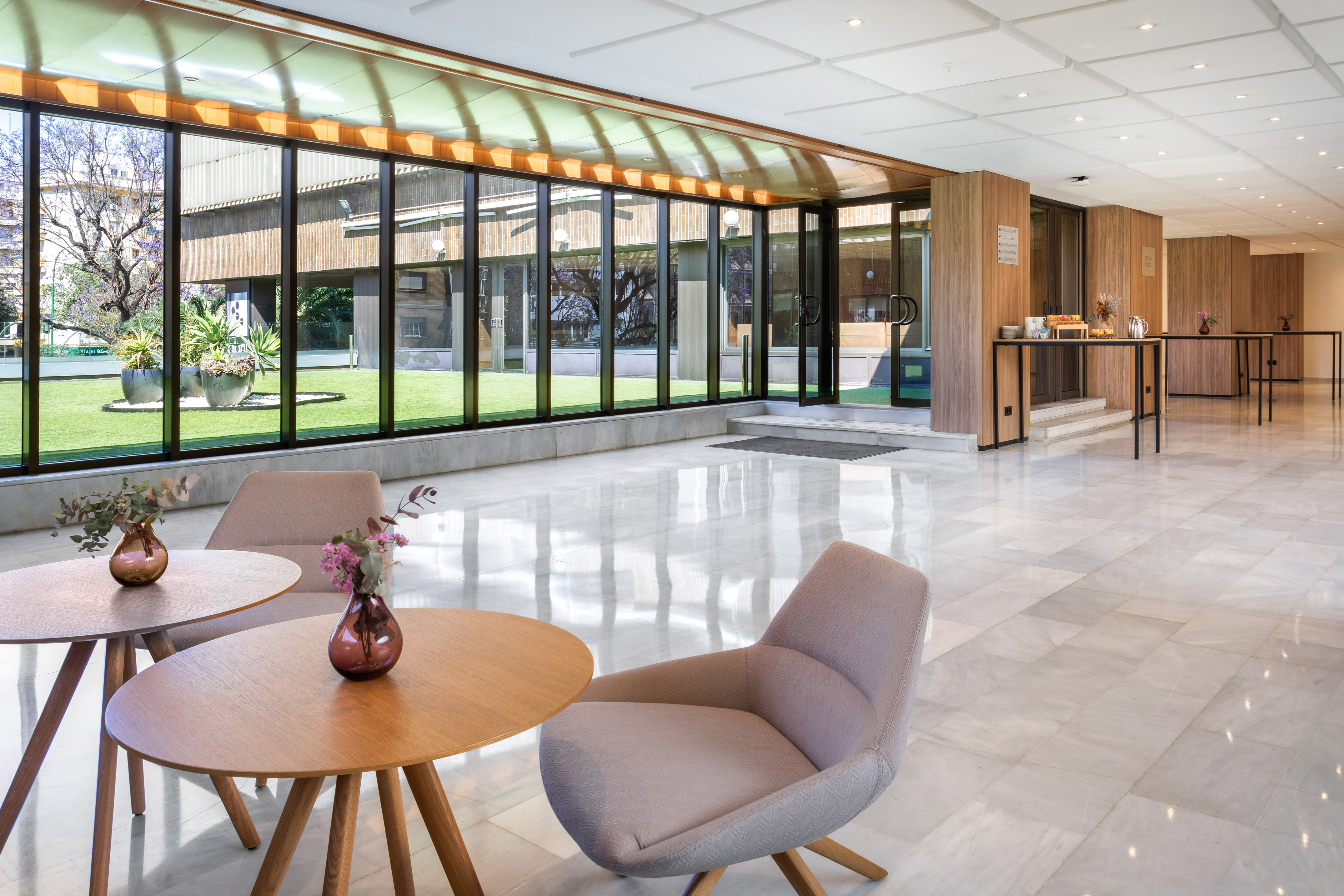 Modern hotel lobby lounge with bright marble floor and lush garden views.