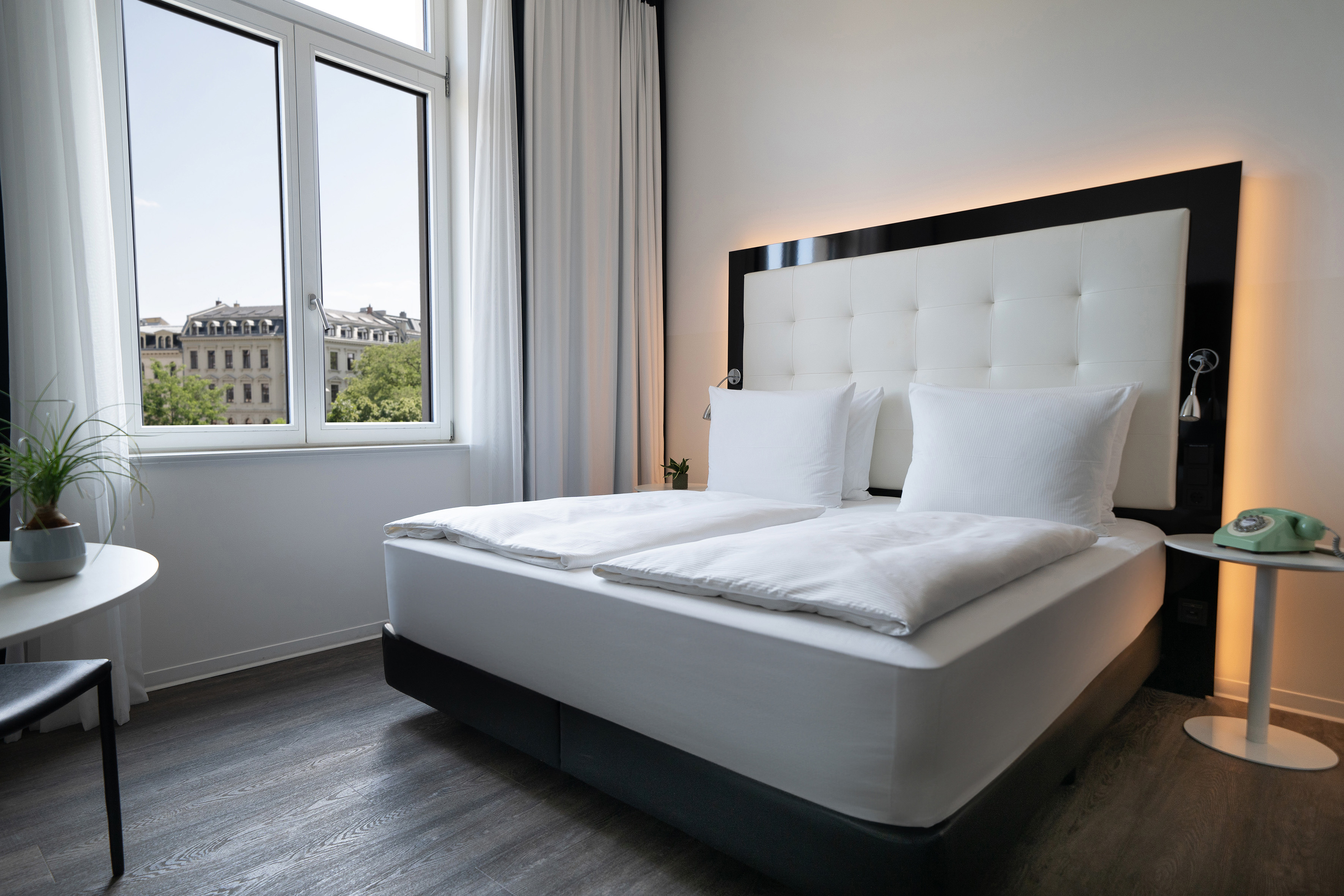 Modern hotel bedroom with large bed, white bedding, and window city view.