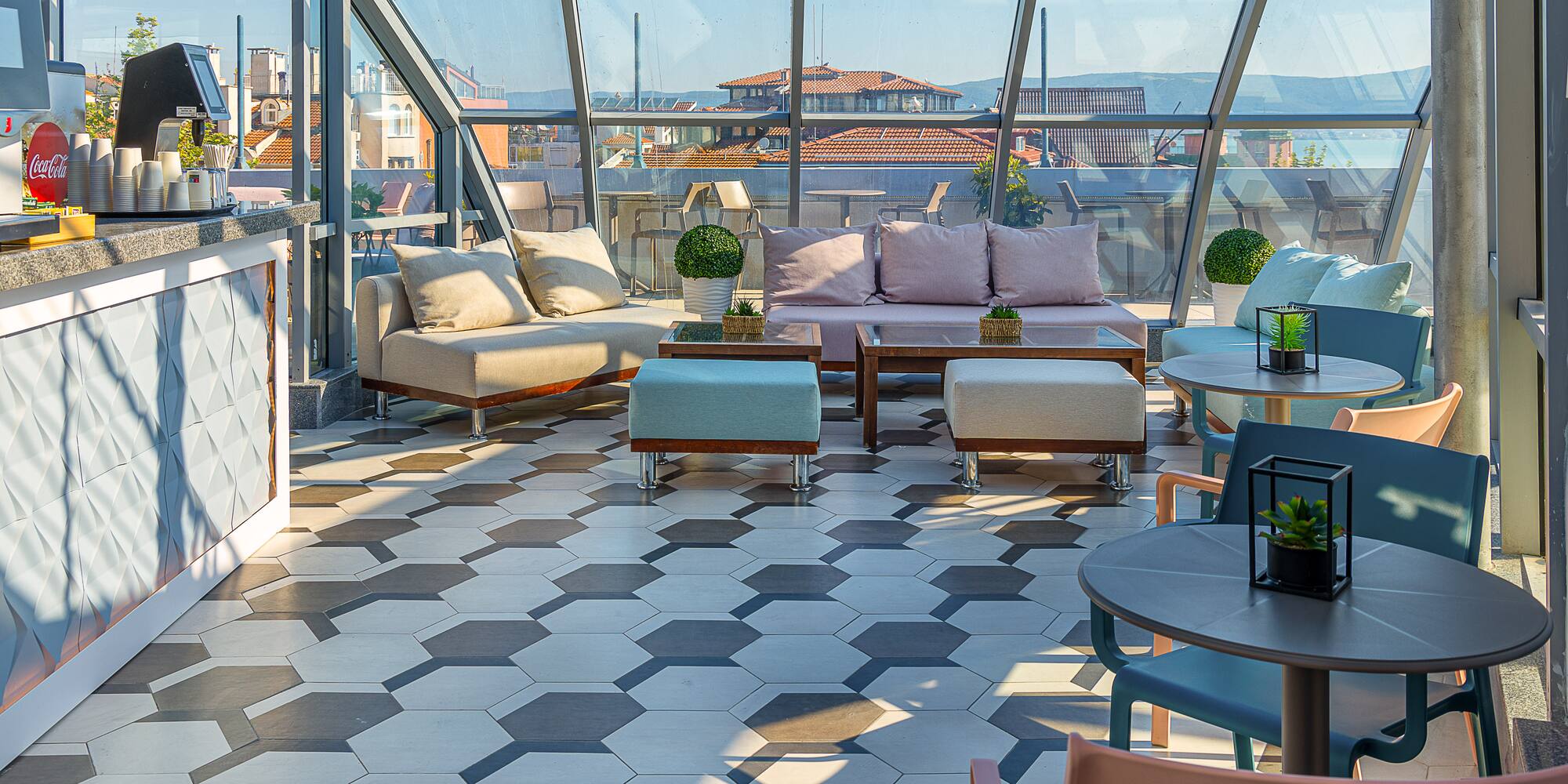 Modern rooftop lounge bar with glass enclosure, hexagon tiles, and city views.