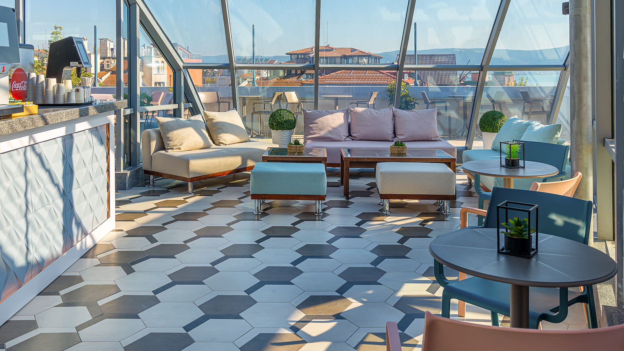 Modern rooftop lounge bar with glass enclosure, hexagon tiles, and city views.