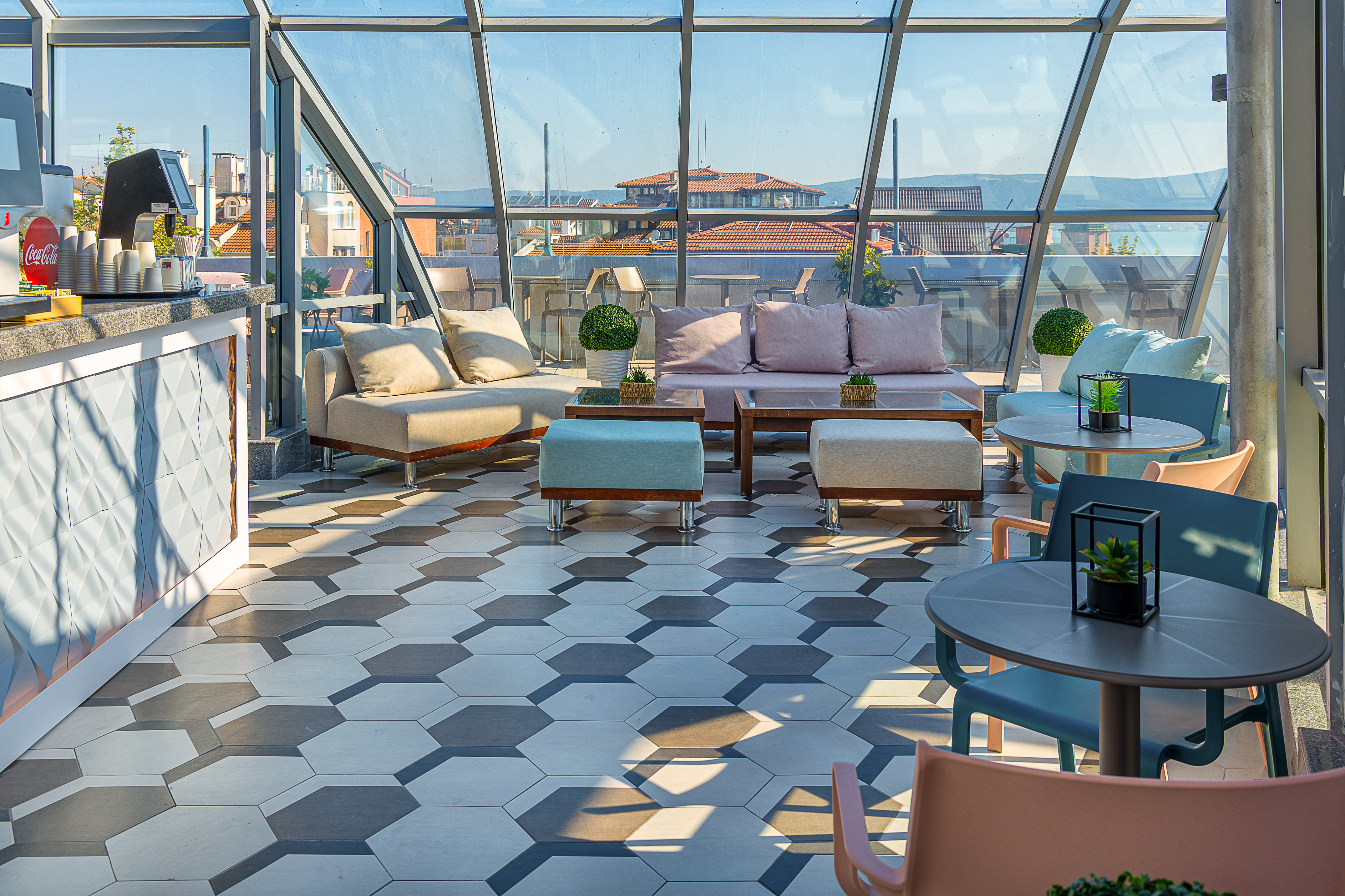 Modern rooftop lounge bar with glass enclosure, hexagon tiles, and city views.